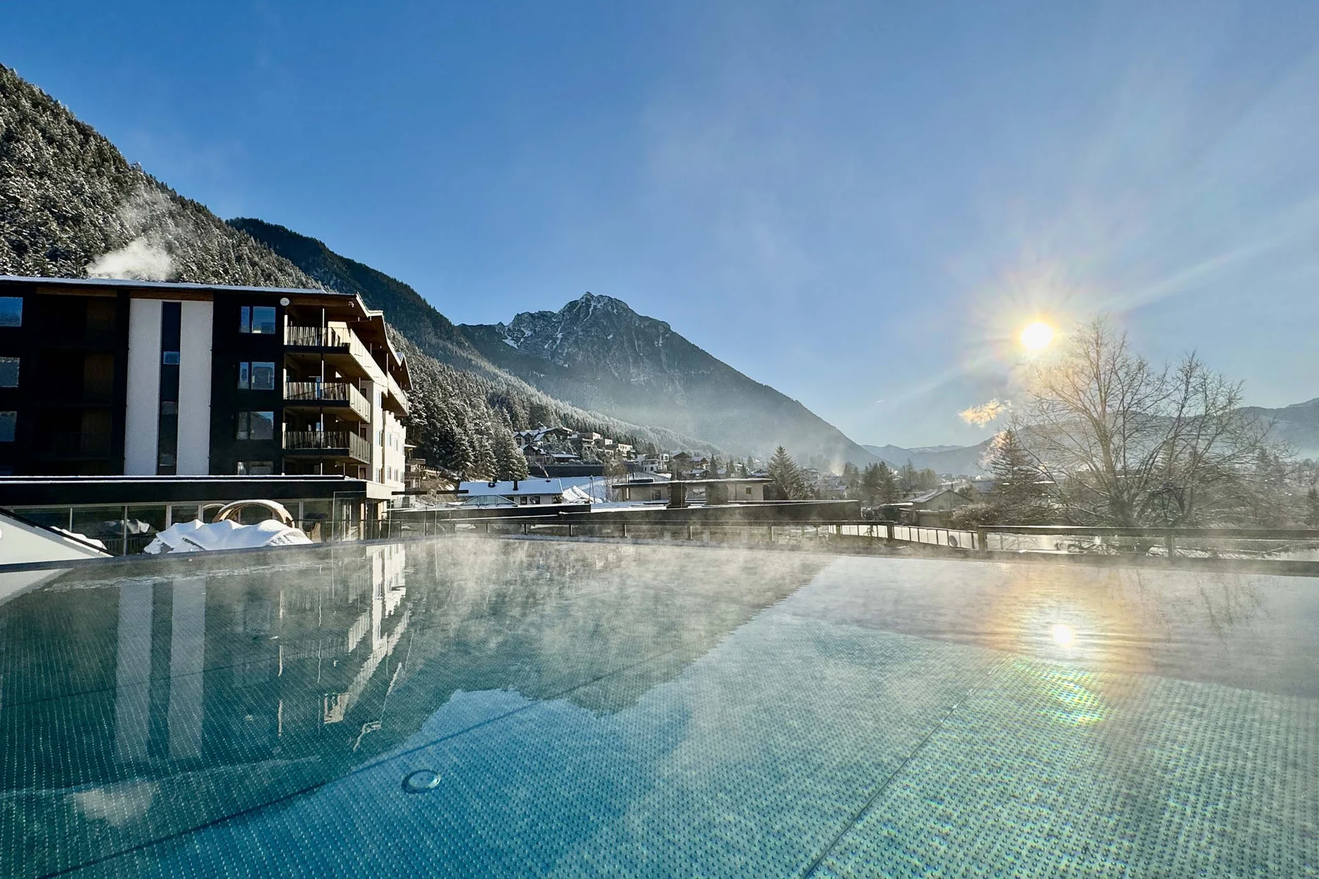 Willkommen im Familienhotel Buchau am Achensee Dampfendes Schwimmbecken mit Berg und Sonne im Hintergrund an einem klaren Wintertag