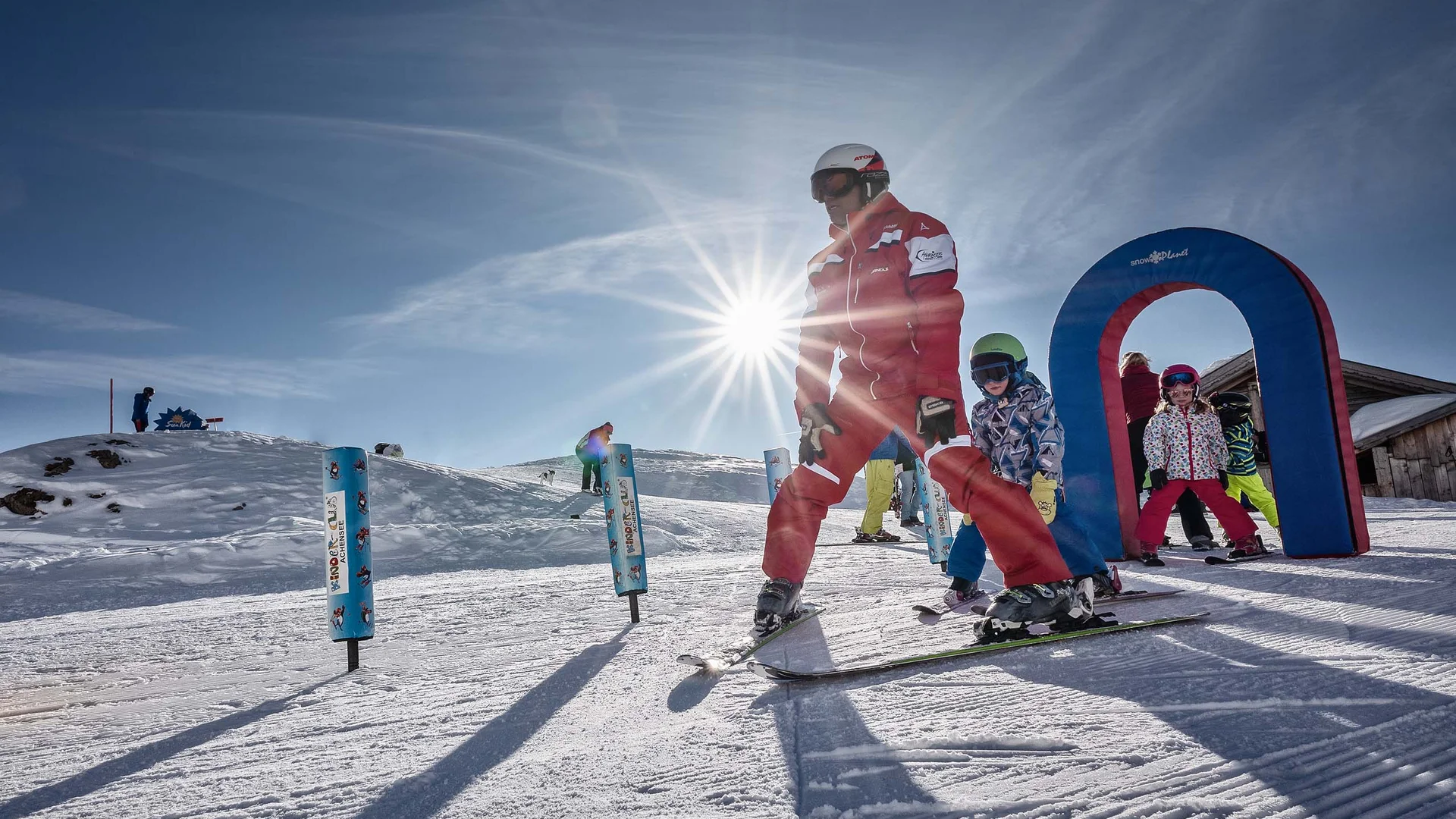 Der Wintertraum im Familien-Skihotel in Österreich Skilehrer mit Kindern beim Skikurs im Schnee an einem sonnigen Tag