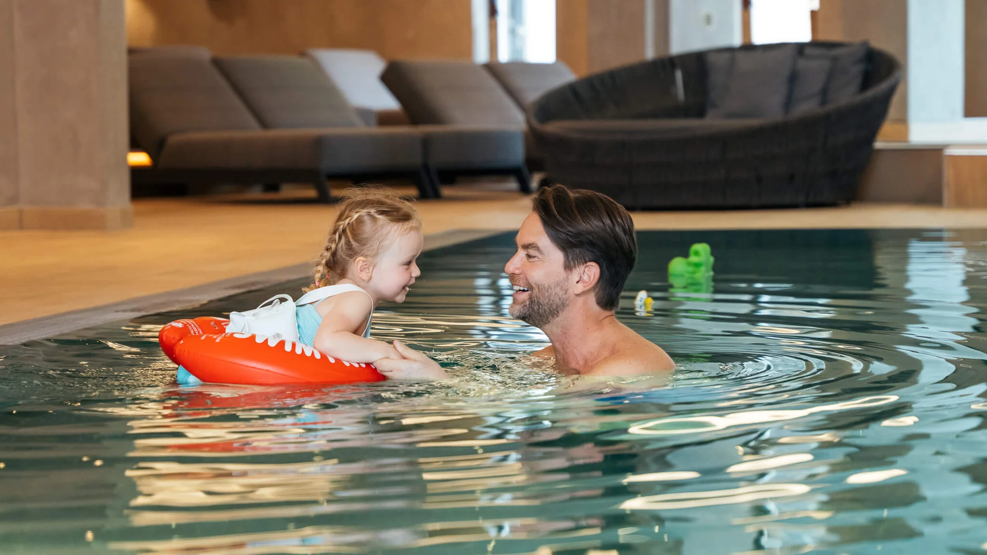 Urlaub im Wellnesshotel mit Kindern in Tirol Mann und Kind mit Schwimmring lächelnd und Händchen haltend im Hallenbad
