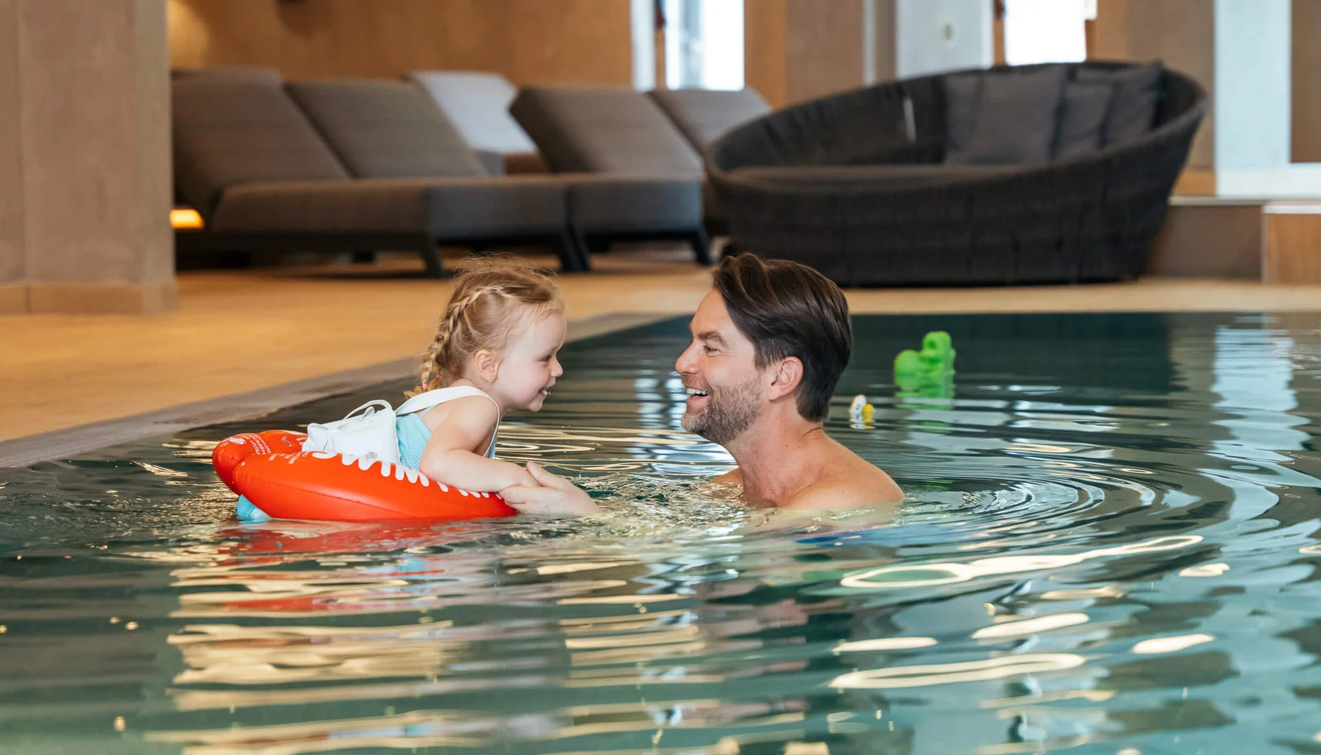 Ab ins Familienhotel mit Schwimmkurs! Mann und Kind mit Schwimmring lächelnd und Händchen haltend im Hallenbad