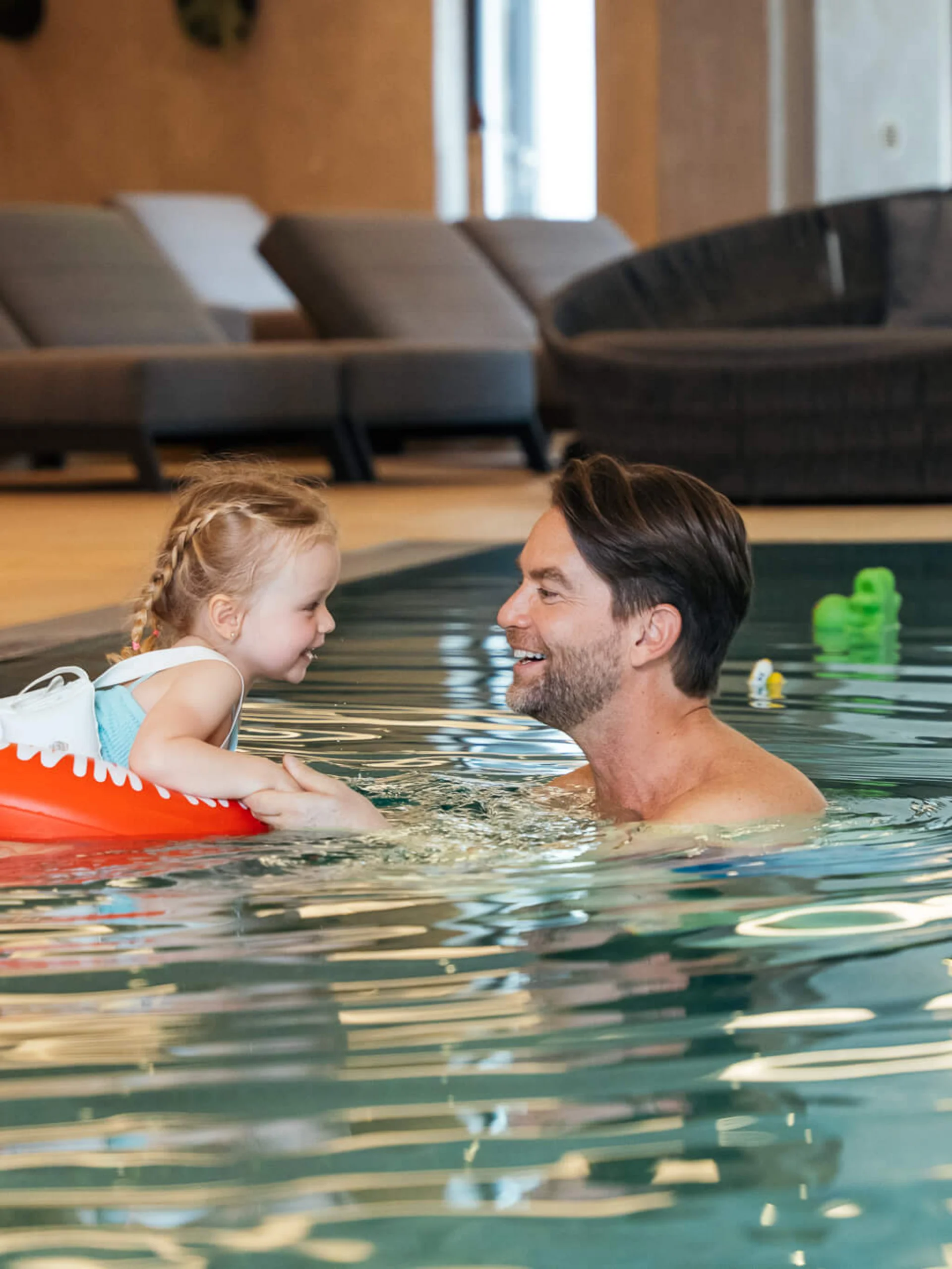 Wir lassen Bilder sprechen. Mann und Kind mit Schwimmring lächelnd und Händchen haltend im Hallenbad