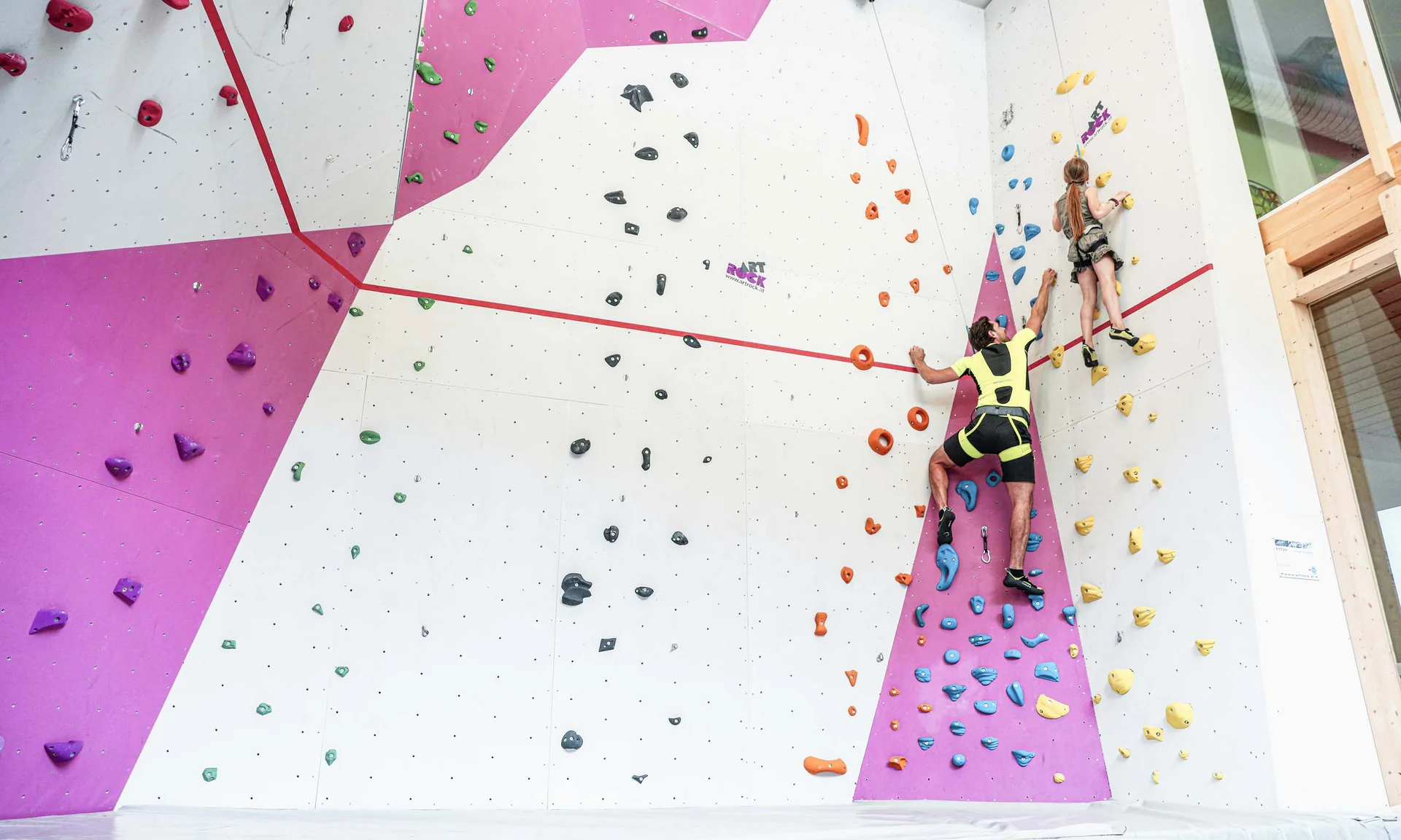 Urlaub im Hotel mit Indoorspielplatz Erwachsener und Kind klettern an farbiger Indoor-Kletterwand