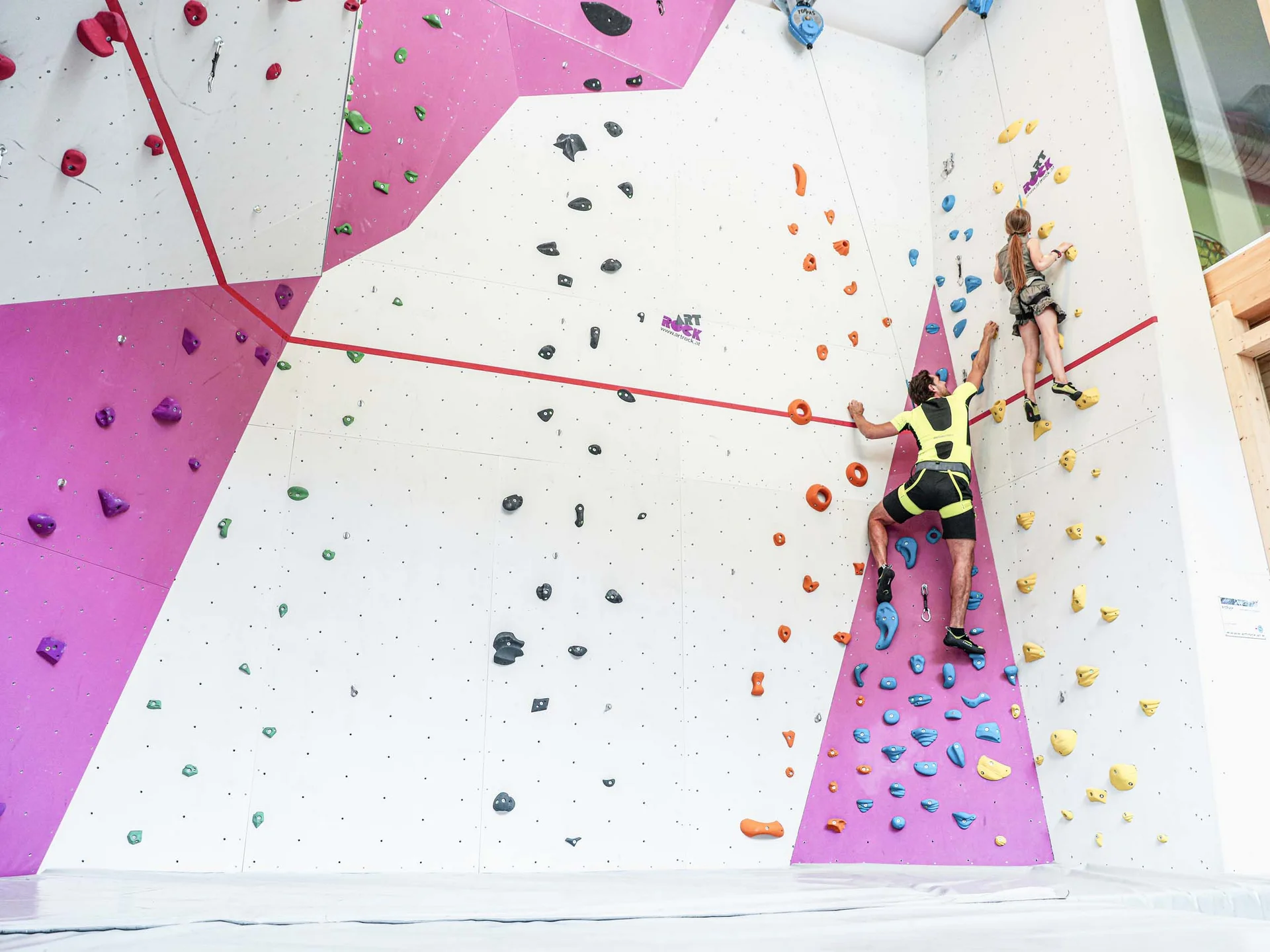 Action im Hotel mit Kletterhalle Erwachsener und Kind klettern an farbiger Indoor-Kletterwand
