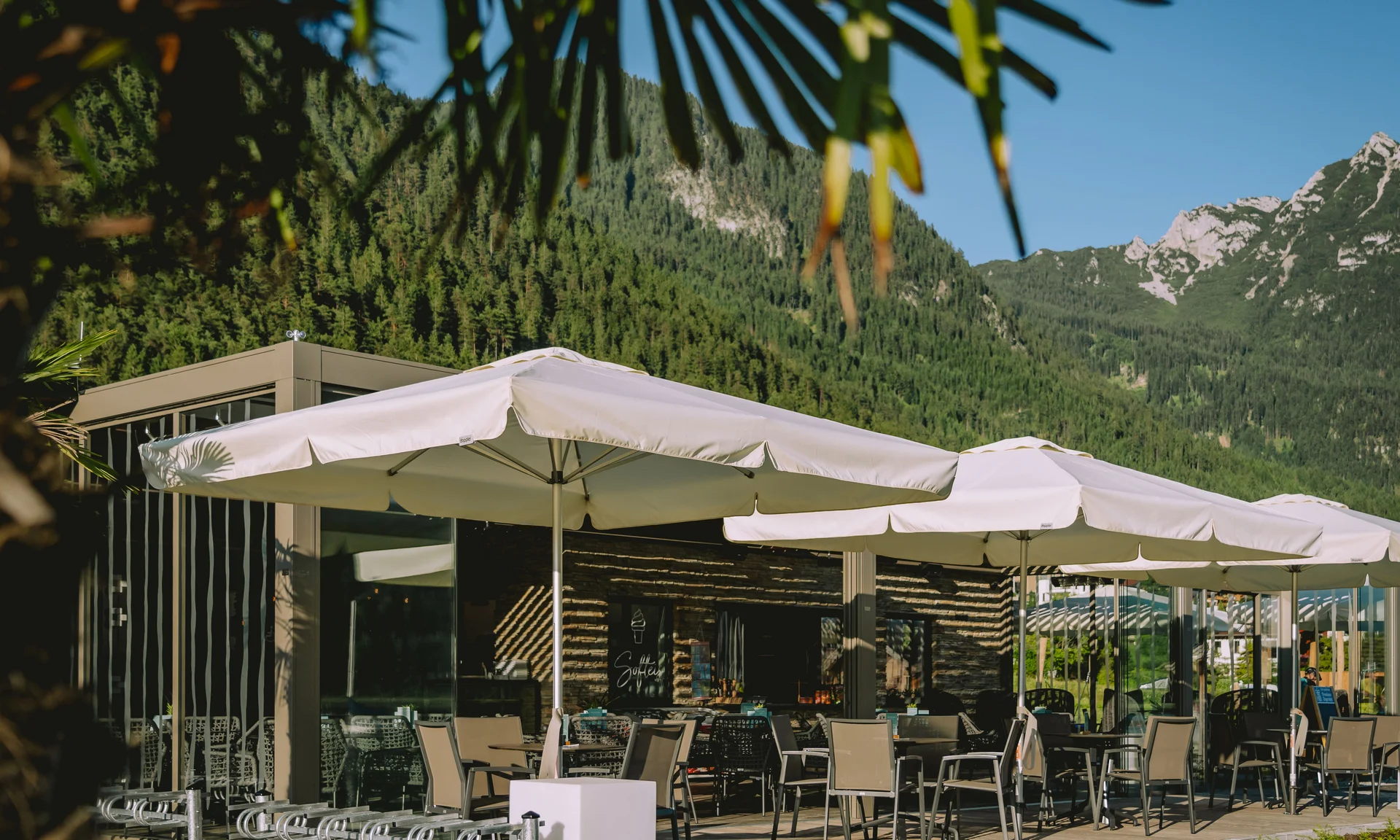 Wir lassen Bilder sprechen. Außenbereich eines Cafés mit Sonnenschirmen und Bergblick