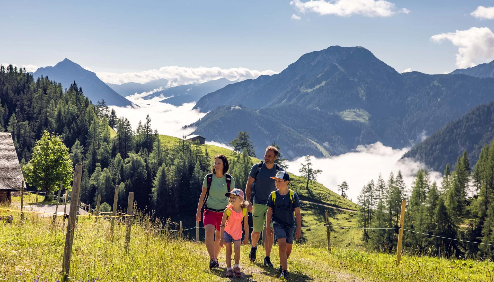 Vom Wanderhotel in Tirol direkt in die Natur Familie wandert auf Bergweg mit Alpenlandschaft und Nebel im Tal
