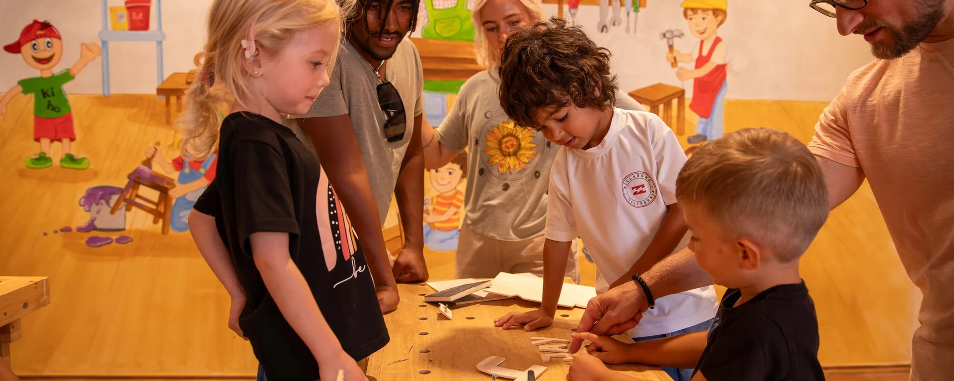 Ihr Hotel mit Kinderbetreuung in Tirol Kinder und Erwachsene arbeiten gemeinsam an einem Holzprojekt in einer Werkstatt