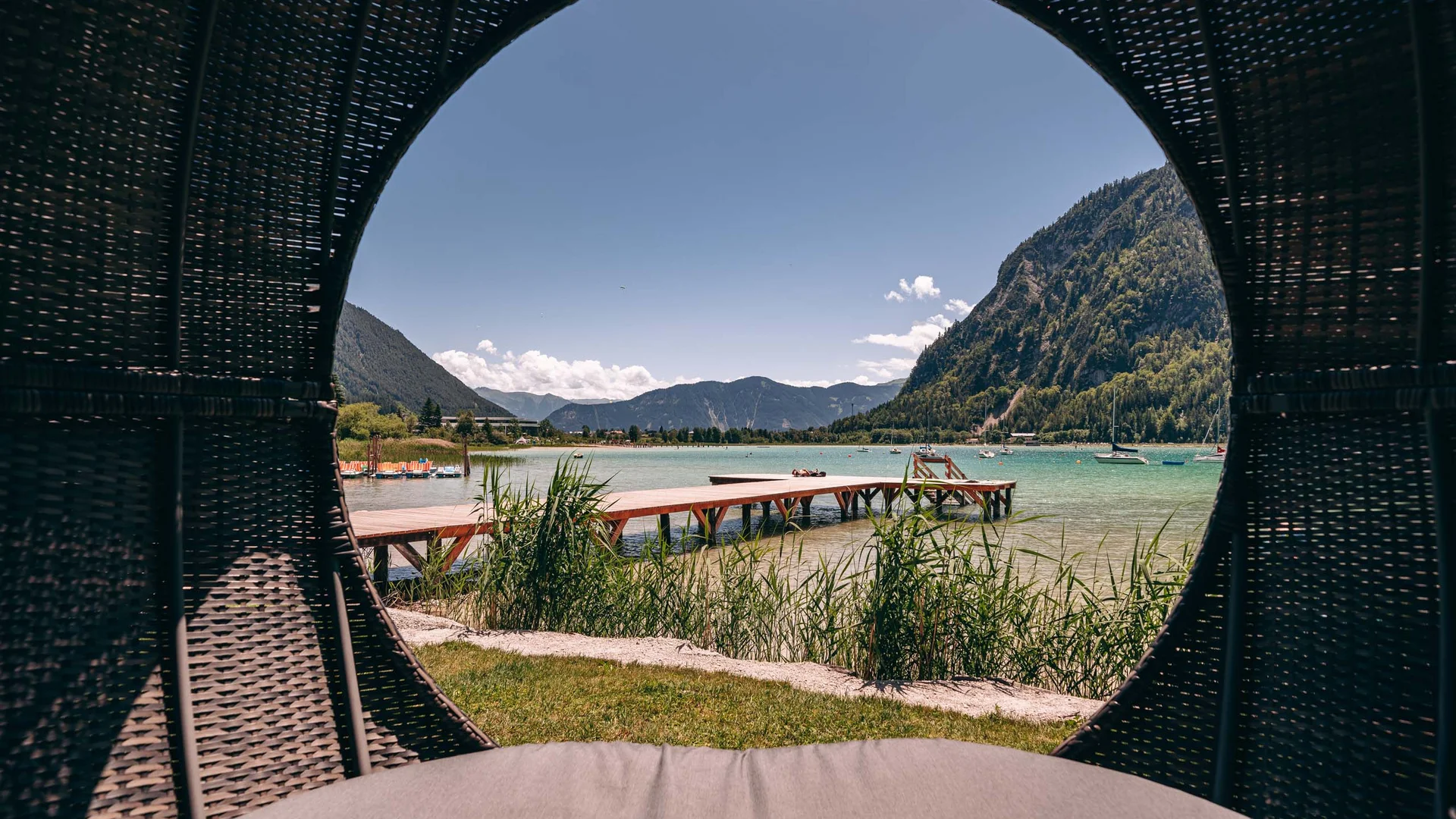 Wassersport auf dem See in Österreich Blick auf einen Steg und Berge durch eine runde Öffnung eines Korbs