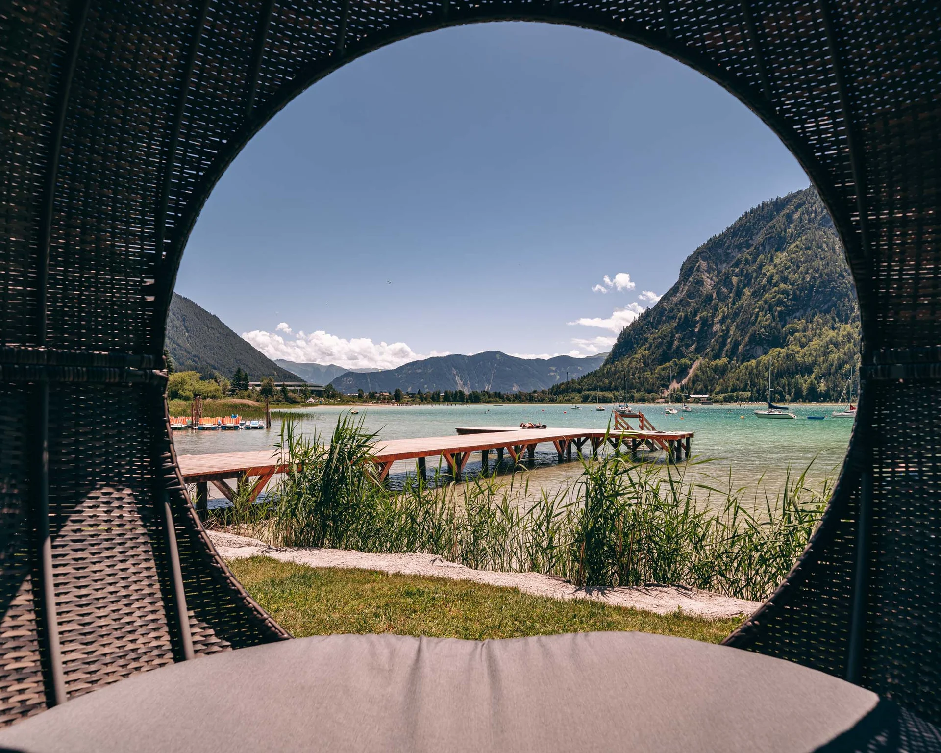 Wassersport auf dem See in Österreich Blick auf einen Steg und Berge durch eine runde Öffnung eines Korbs