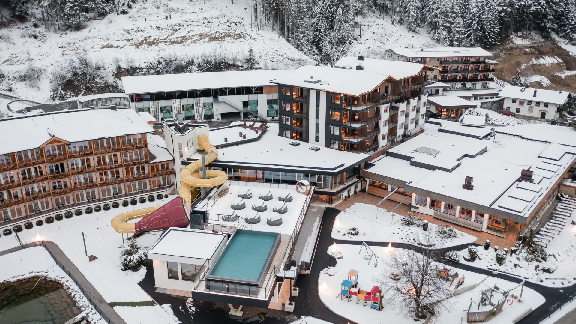 Urlaub im Wellnesshotel mit Kindern in Tirol Vogelperspektive auf ein schneebedecktes Hotel mit Wasserrutsche im Winter