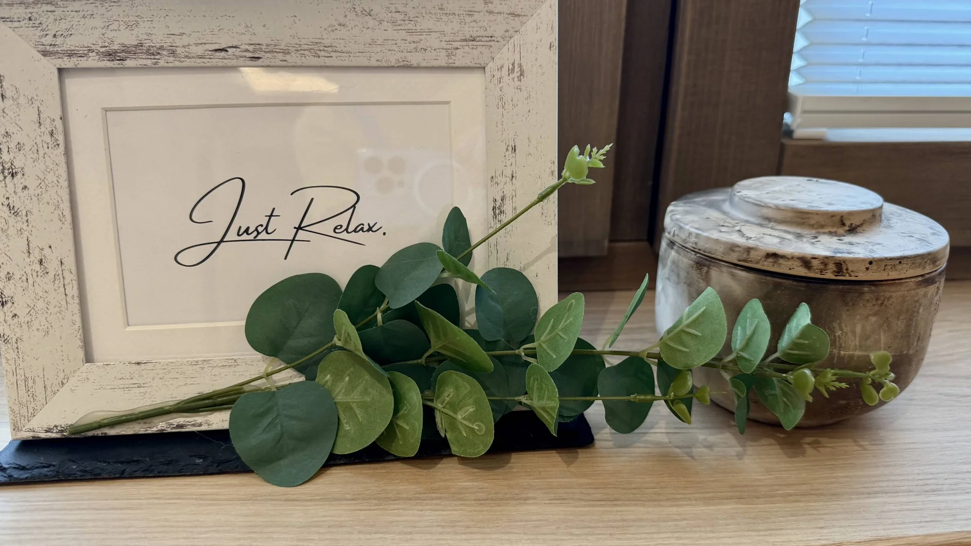 Urlaub im Wellnesshotel mit Kindern in Tirol Bilderrahmen mit Text Just Relax, grüne Blätter und eine Keramikdose auf Holzregal