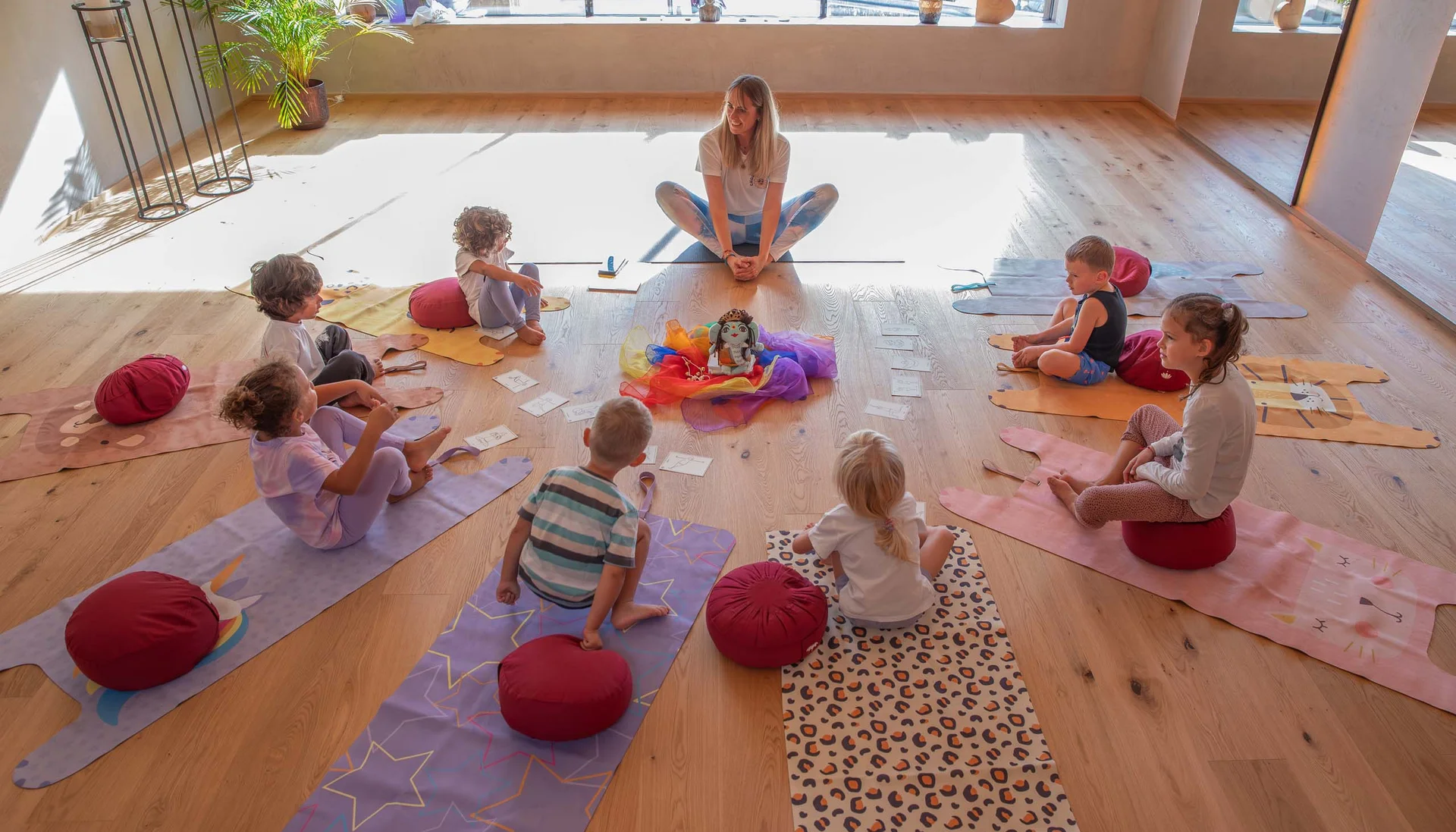 Fitness und Yoga im Hotel in Tirol Kinder und Lehrerin sitzen im Kreis auf Yogamatten in einem hellen Raum