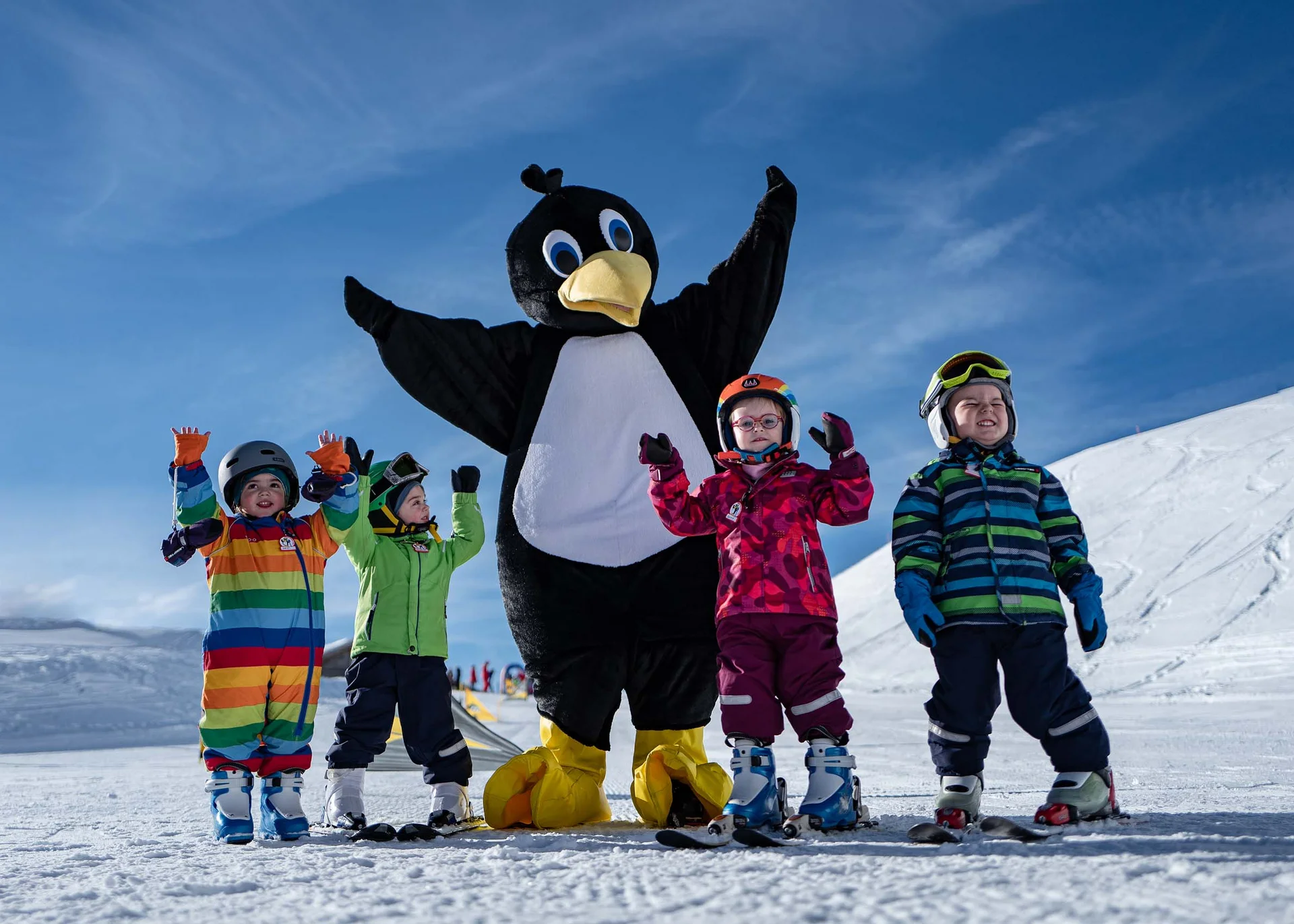 Der Wintertraum im Familien-Skihotel in Österreich Kinder mit Skiausrüstung posieren neben einer Person im Pinguin-Kostüm im Schnee