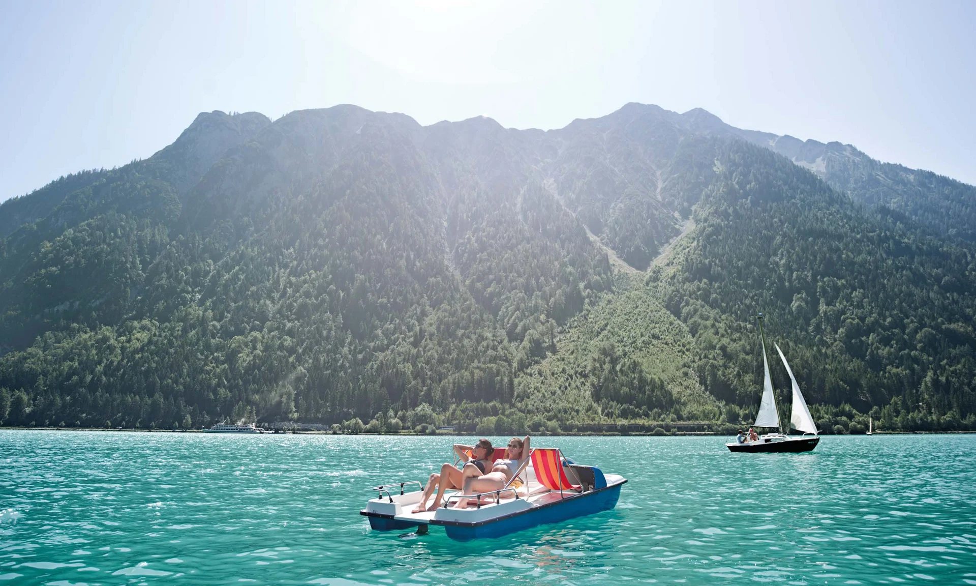 Freizeitkurse für Ihre Kids und Teenies Zwei Personen sonnen sich auf einem Tretboot auf einem See vor bewaldeten Bergen