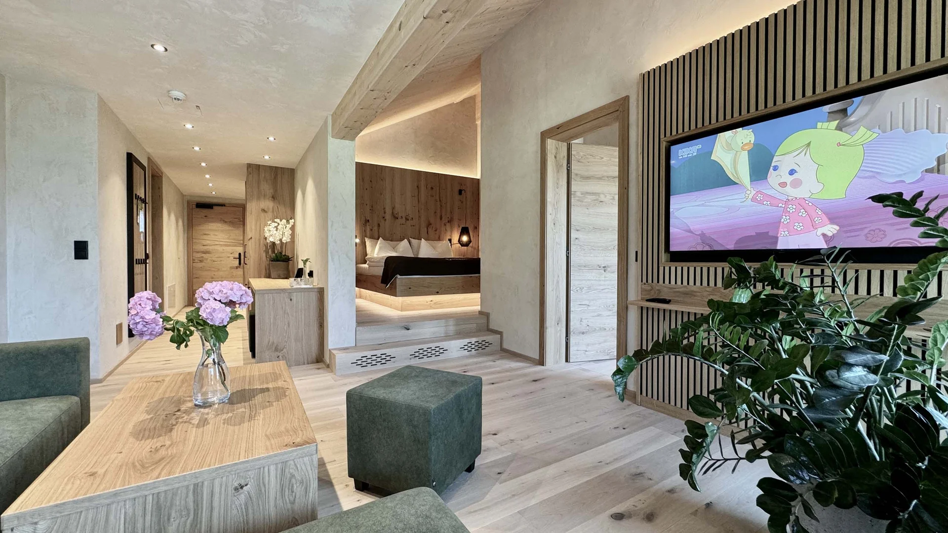 Zimmer und Angebote am Achensee Moderner Hotelwohnraum mit grünem Sofa, TV und Schlafzimmer im Hintergrund