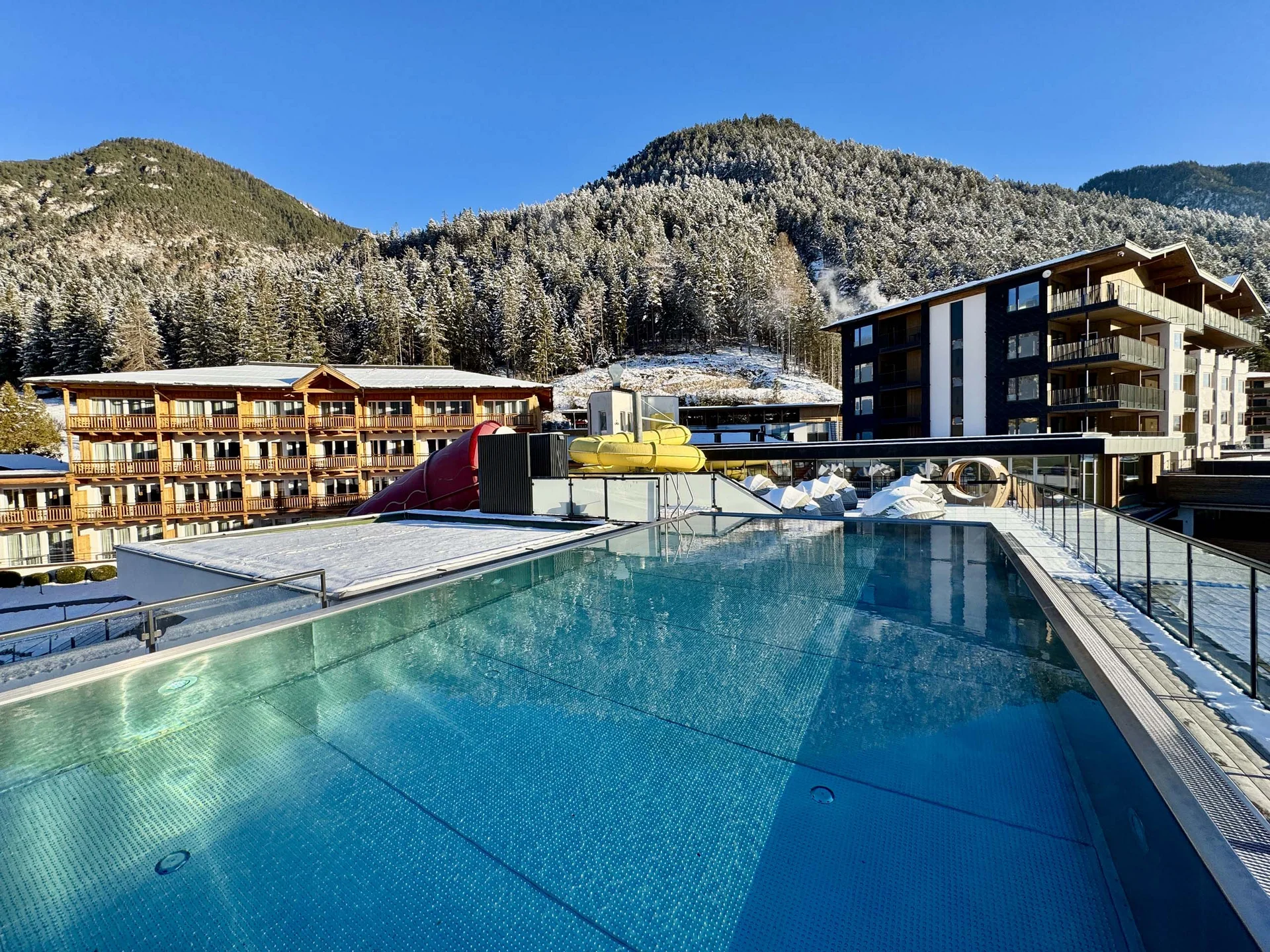 Urlaub im Wellnesshotel mit Kindern in Tirol Schwimmbad auf der Dachterrasse mit verschneiten Bergen und Hotels im Hintergrund