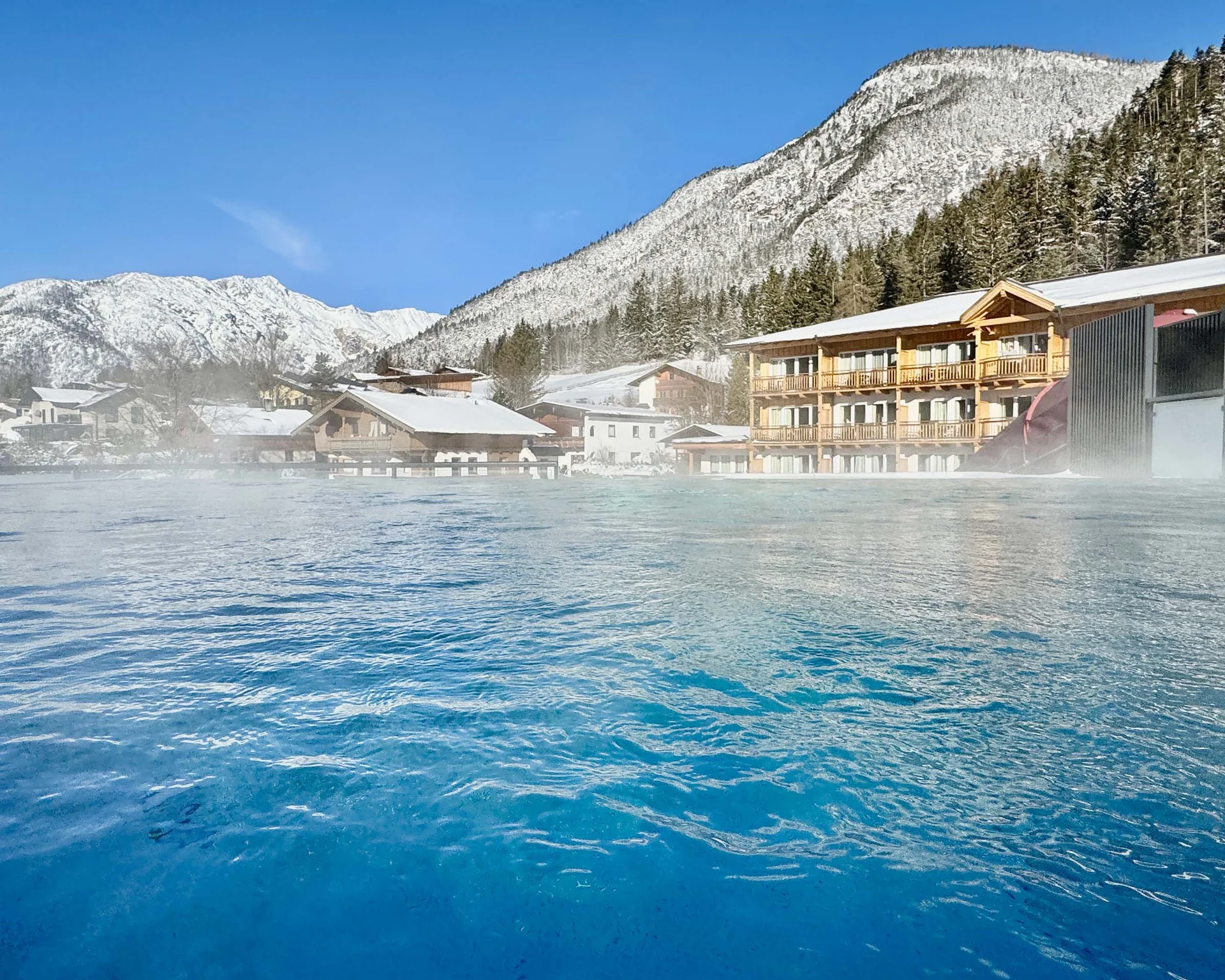 Willkommen im Familienhotel Buchau am Achensee Outdoor-Hallenbad mit Bergblick und schneebedeckten Häusern im Winter
