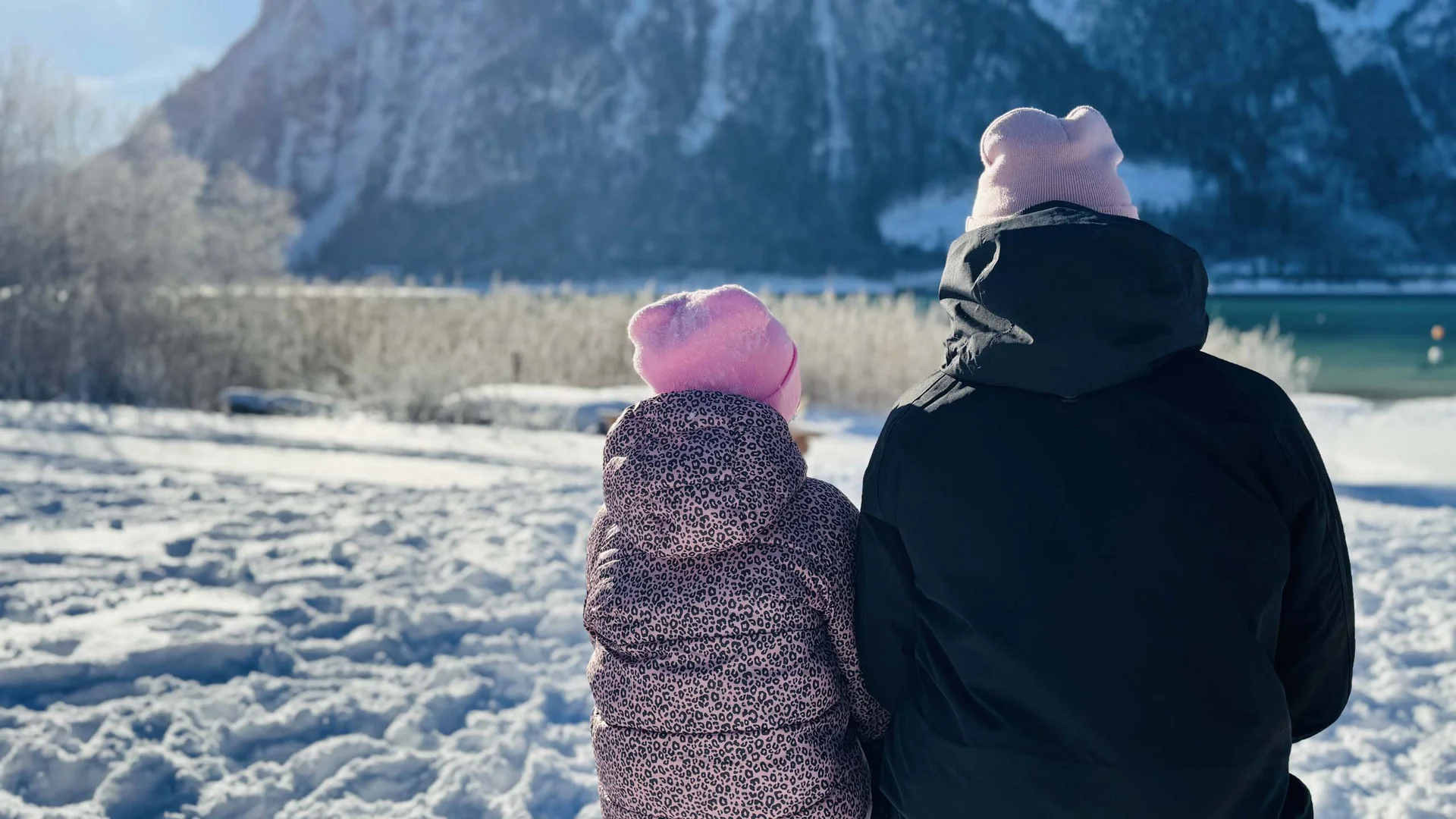 Willkommen im Familienhotel Buchau am Achensee Zwei Personen mit Mützen sitzen im Schnee und blicken auf verschneite Berge