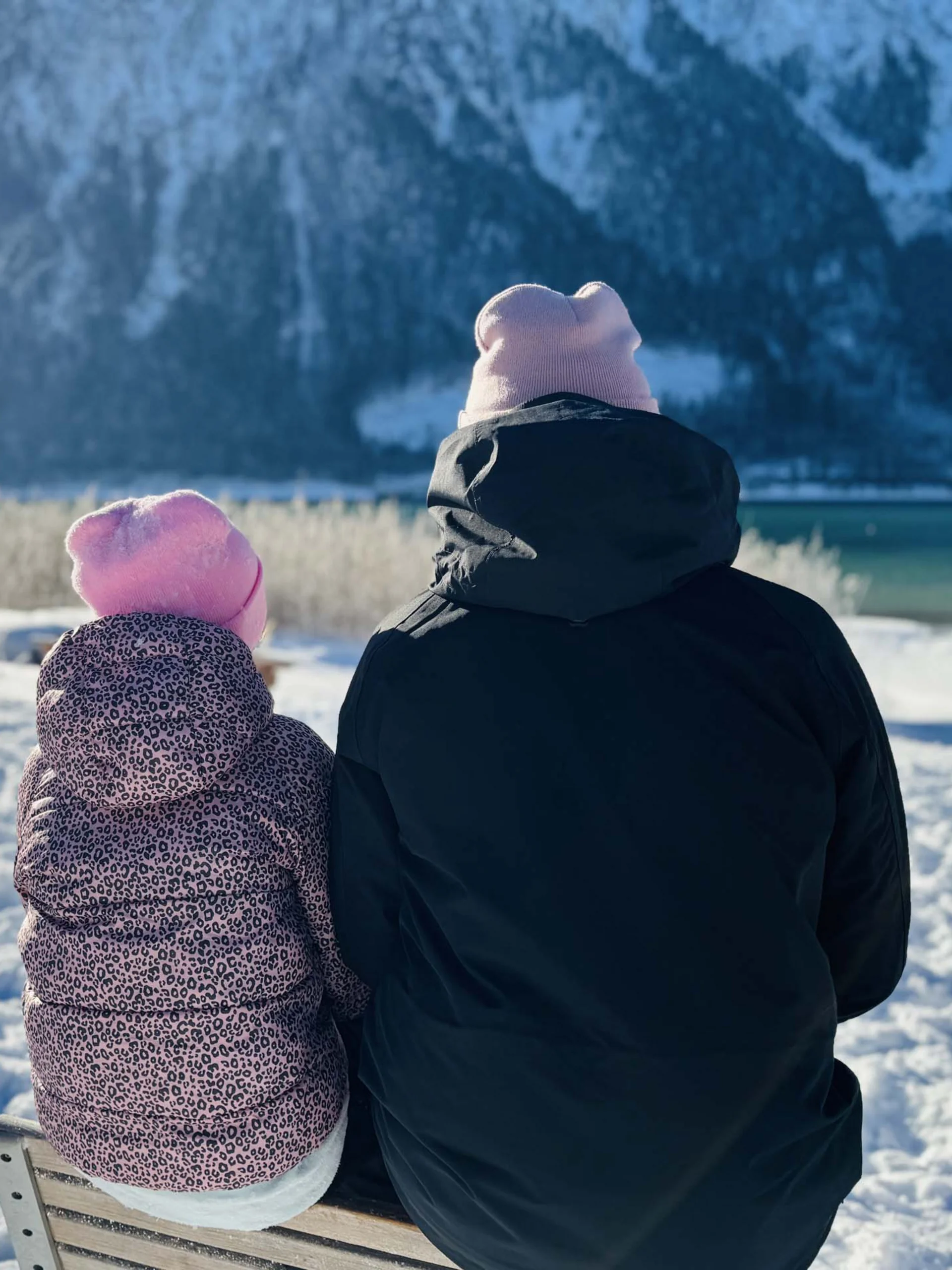 Willkommen im Familienhotel Buchau am Achensee Zwei Personen mit Mützen sitzen im Schnee und blicken auf verschneite Berge