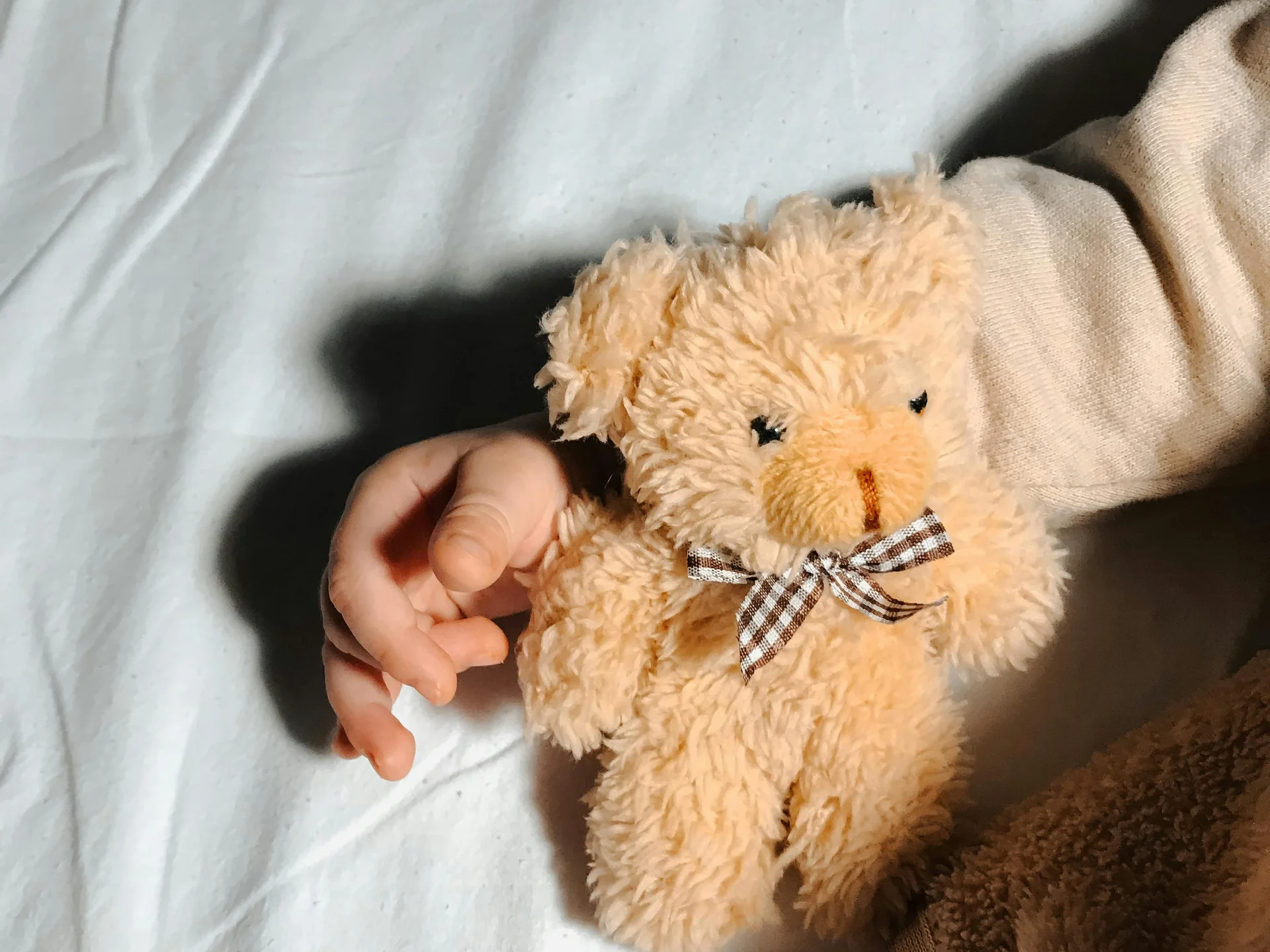 Familienurlaub mit Baby und Kleinkind im Buchau Hand hält kleinen beigen Teddybär mit gestreiftem Schleifenband auf weißem Stoff