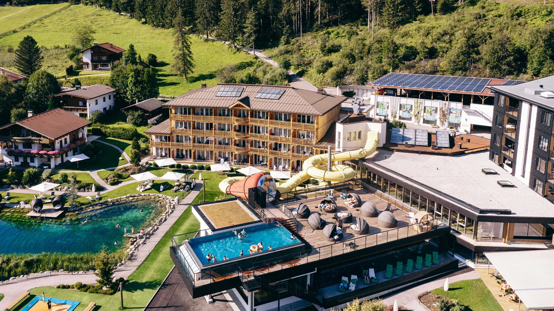 Welcome to our family hotel at Lake Achensee. Hotel complex with pool, waterslide, and sauna in a forested area