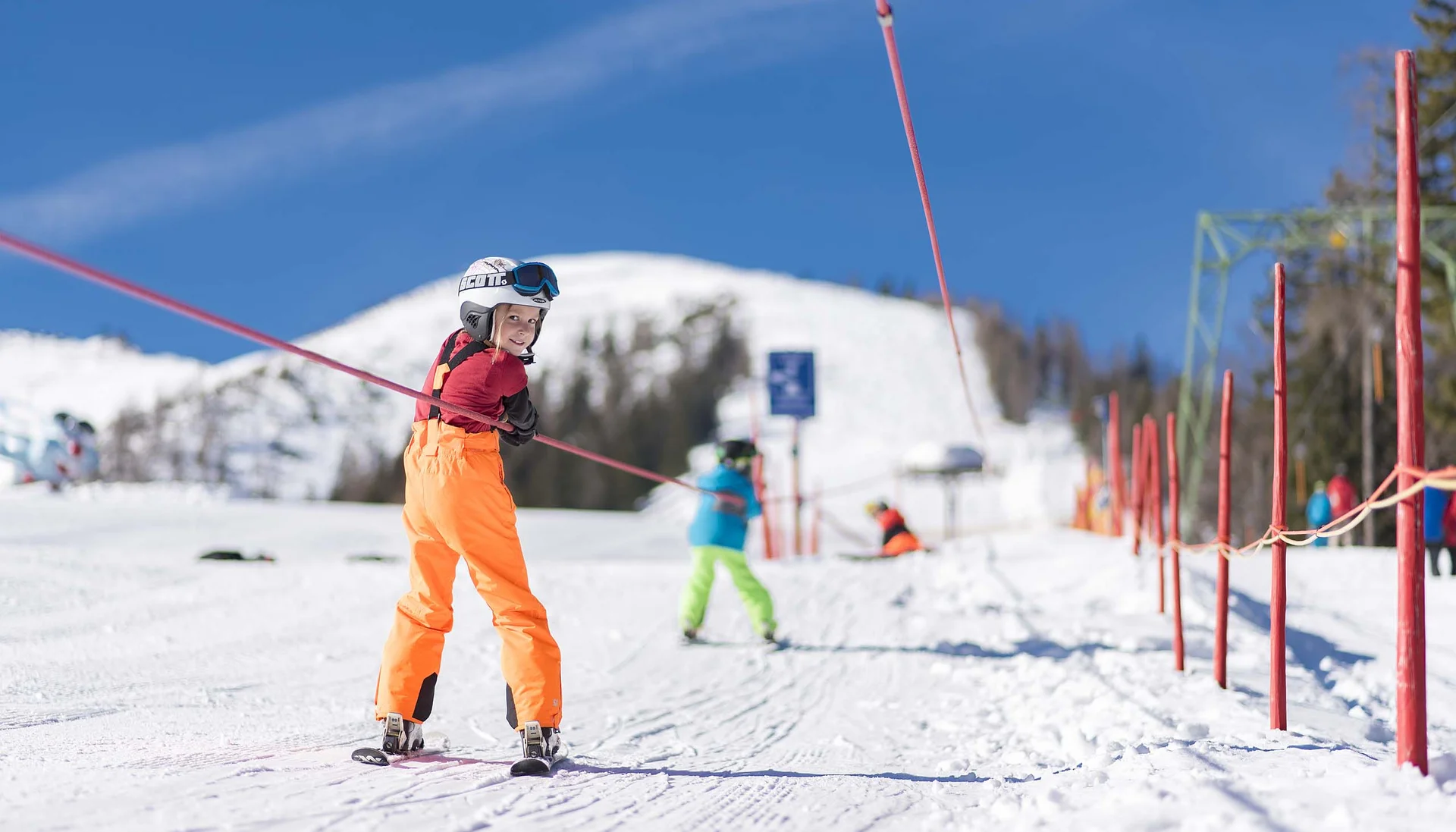 Der Wintertraum im Familien-Skihotel in Österreich Kind in orange Skihose fährt an einem Skilift am sonnigen Schneehang