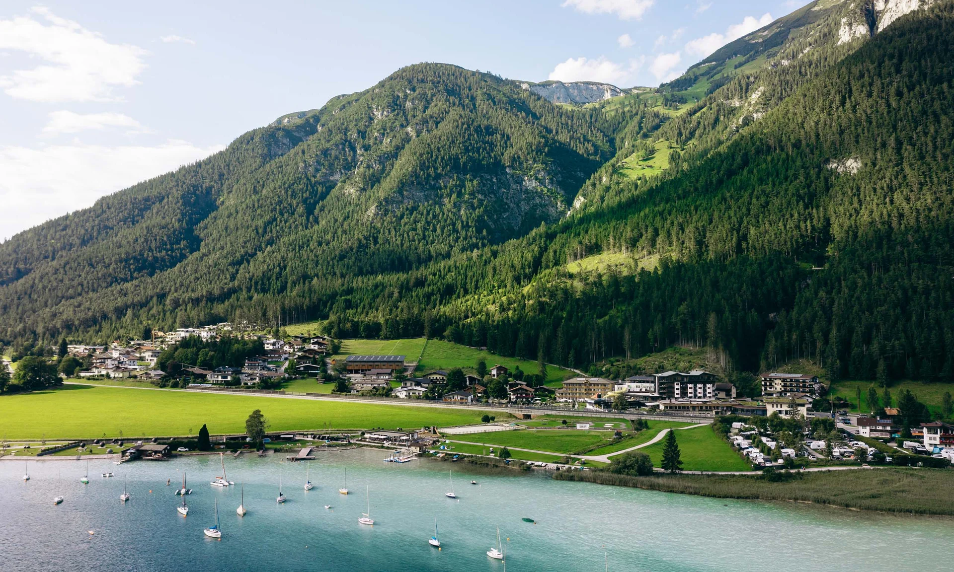 Wassersport auf dem See in Österreich Dorf am See mit Segelbooten und bewaldeten Bergen im Hintergrund