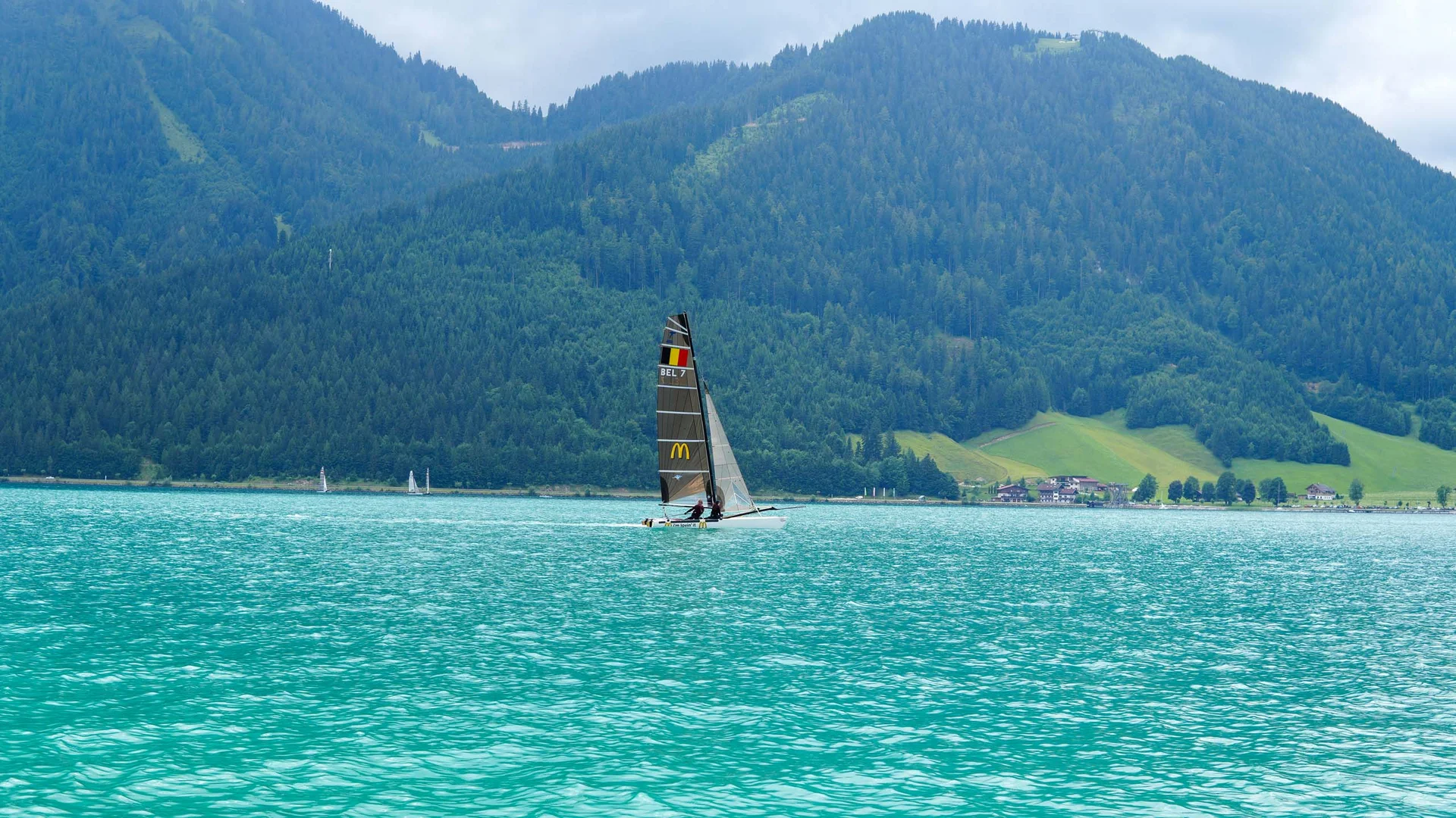 Wassersport auf dem See in Österreich Segelboot auf türkisfarbenem See vor bewaldeten Bergen