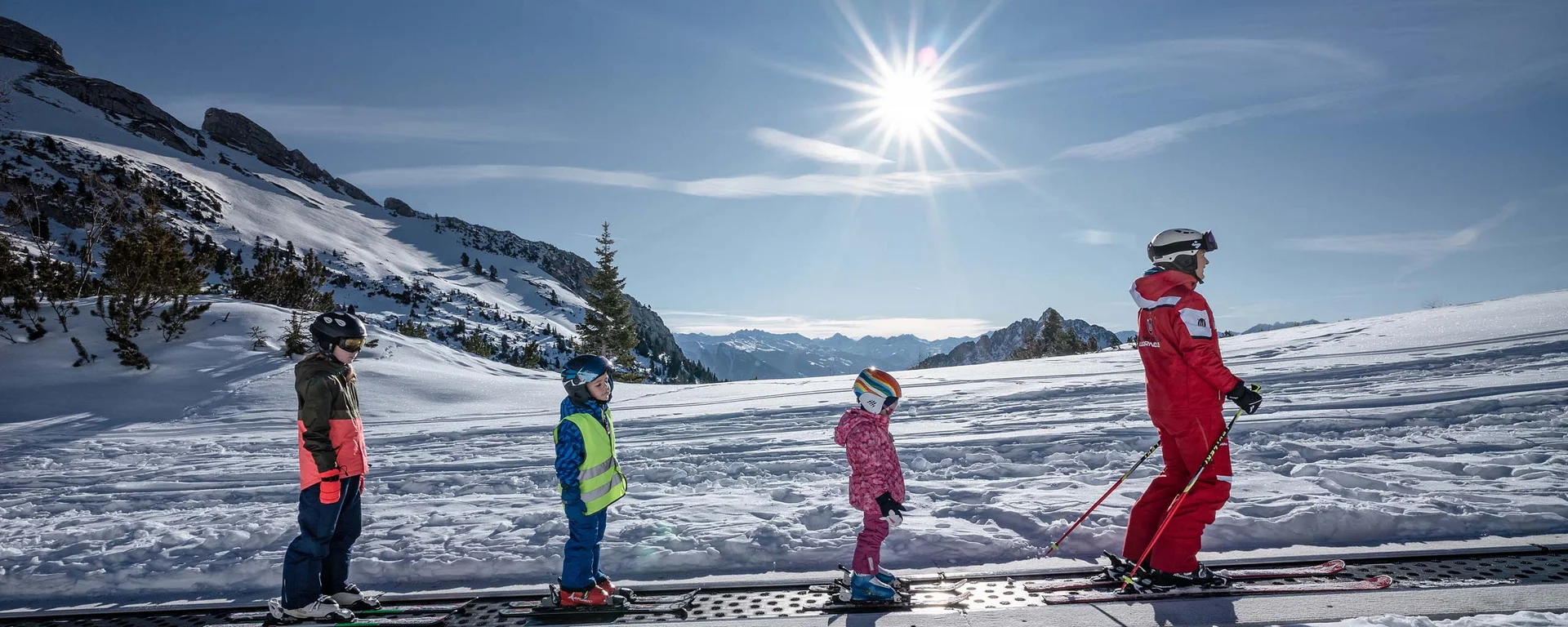 Ihr abenteuerlicher Erlebnisurlaub in Österreich Kinder und Skilehrer auf Förderband im Skigebiet bei sonnigem Winterwetter