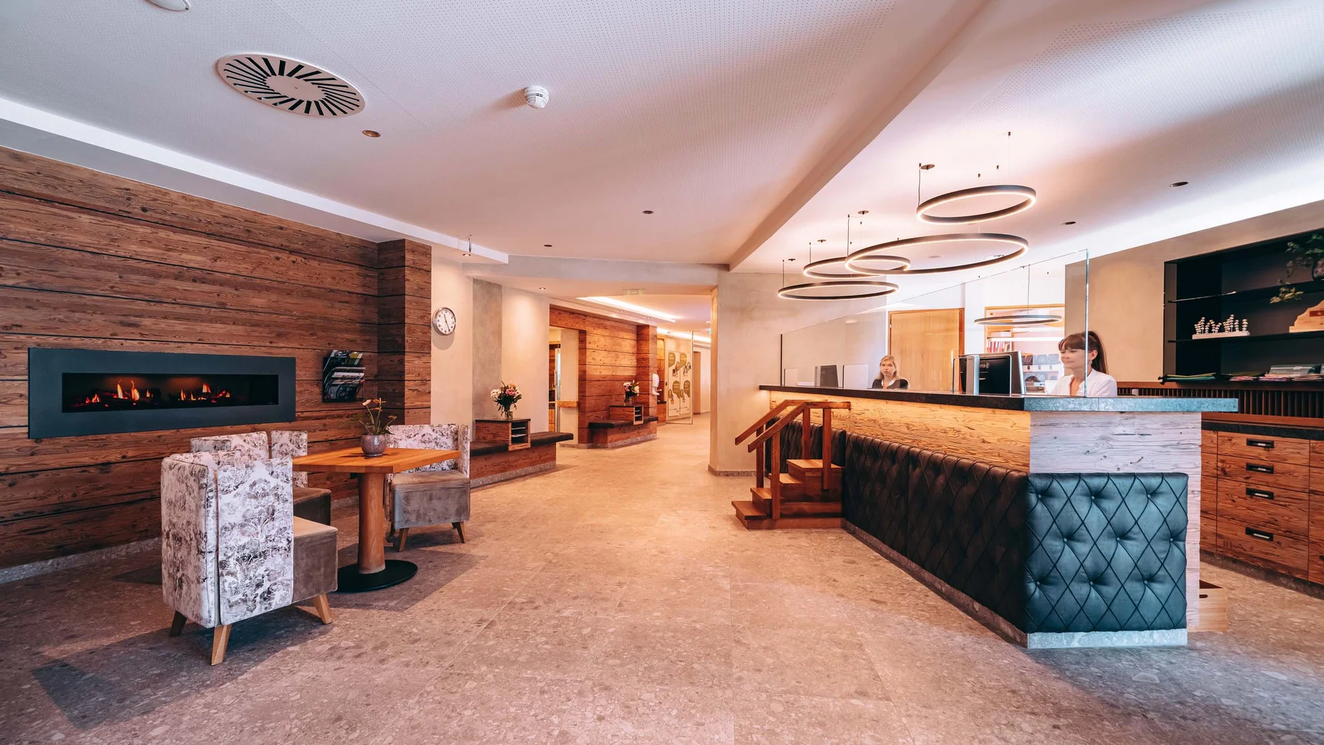 Stammgast werden und Buchau-Taler sammeln Moderner Hotellobby mit Rezeption, Sitzbereich und Kamin an Holzwand