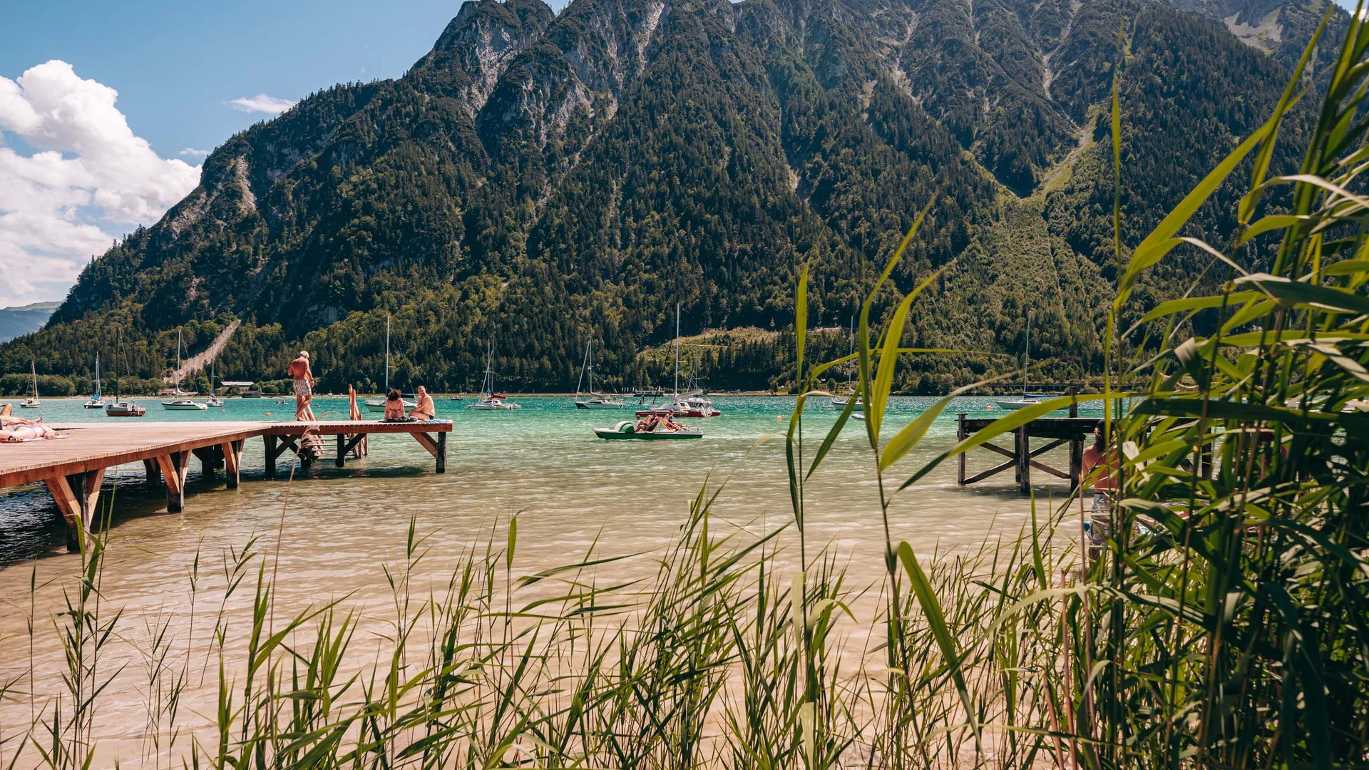 Ihr Familienhotel in Österreich mit All-inclusive-Angebot See mit Stegen, Segelbooten und Bergen im Hintergrund bei sonnigem Wetter