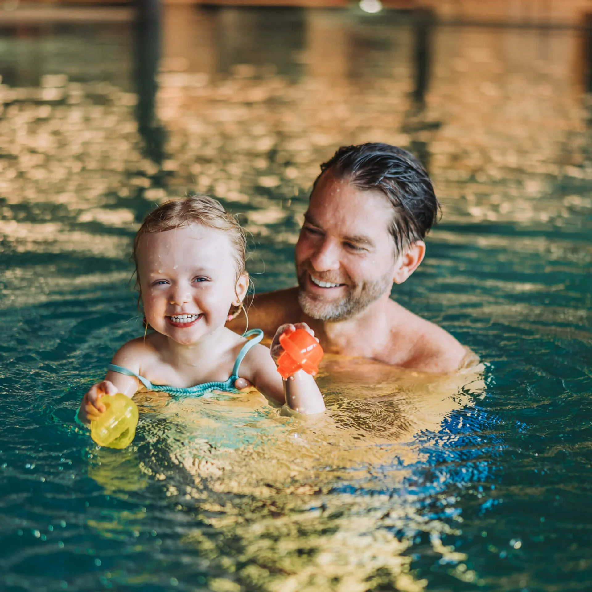 Familienurlaub mit Baby und Kleinkind im Buchau Lachendes Kleinkind mit Vater im Schwimmbad mit bunten Spielzeugen