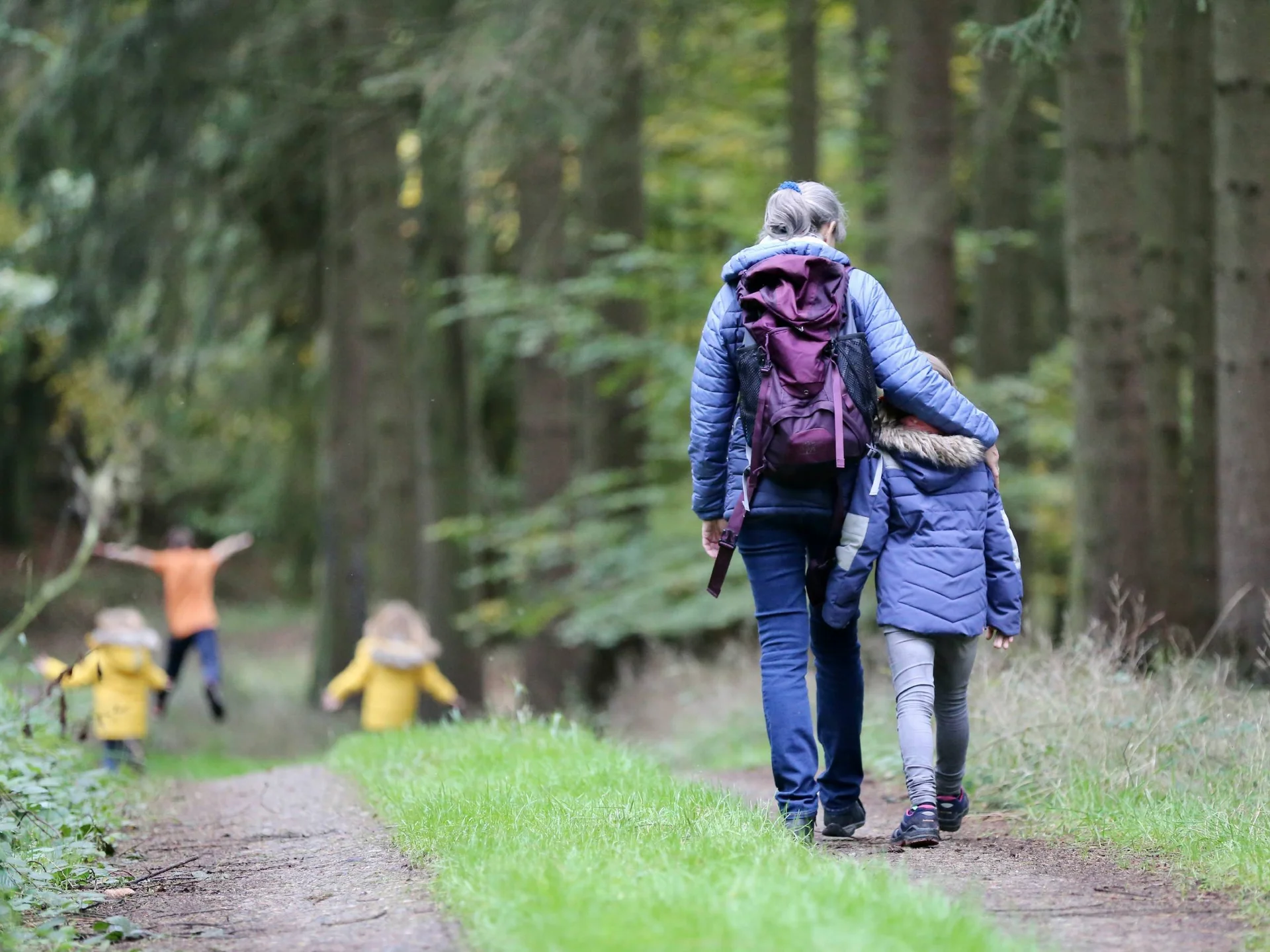 Ihr langersehnter Urlaub mit Enkelkind Frau mit Kind beim Spaziergang im Wald, andere Kinder spielen im Hintergrund