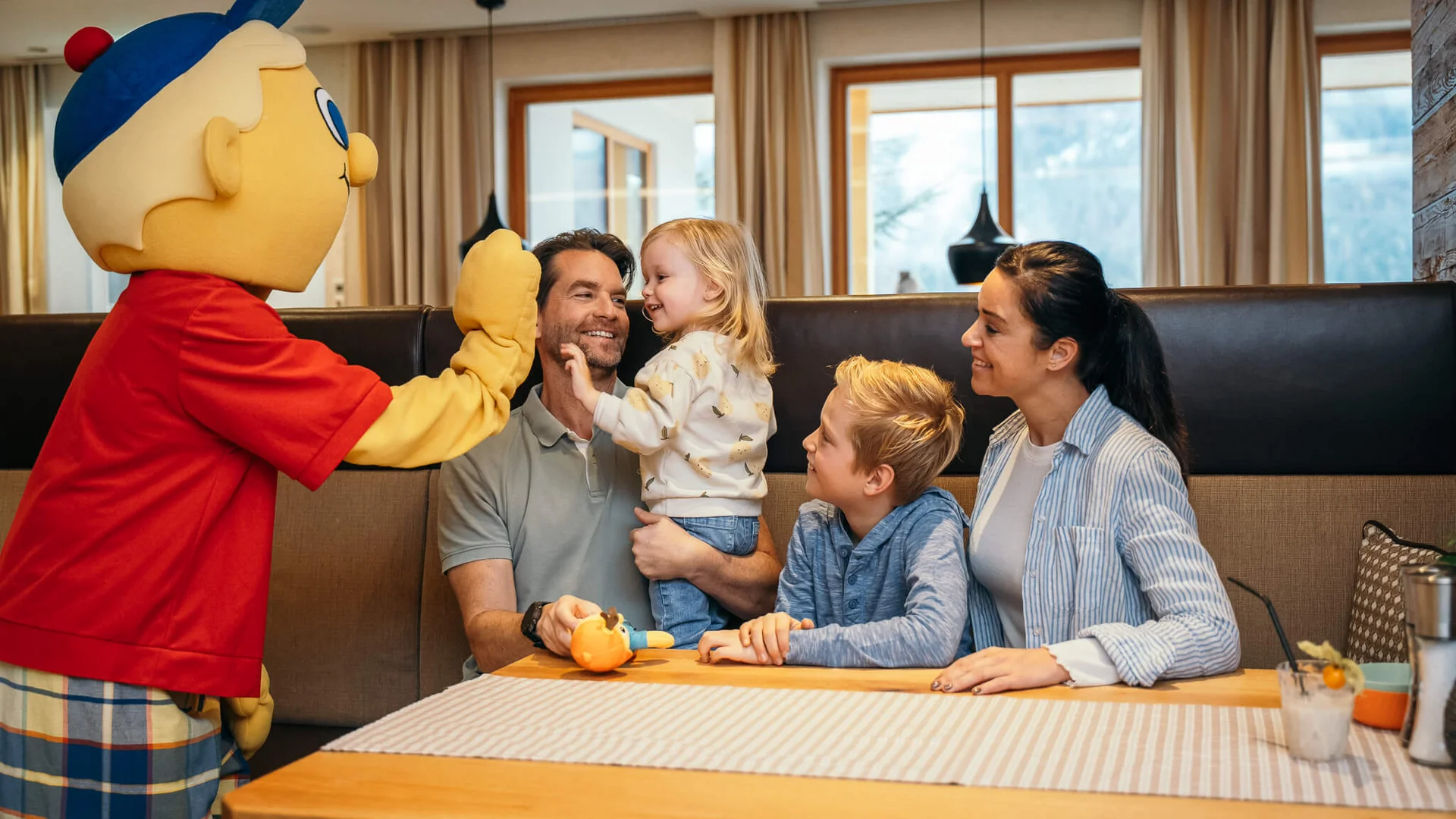Ihr Familienhotel in Österreich mit All-inclusive-Angebot Familie mit zwei Kindern trifft eine Person in einer bunten Cartoon-Figur Kostüm