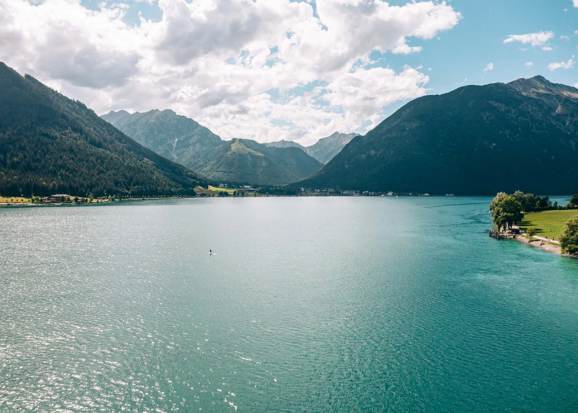 Welcome to our family hotel at Lake Achensee. Blue mountain lake surrounded by forested mountains under cloudy sky