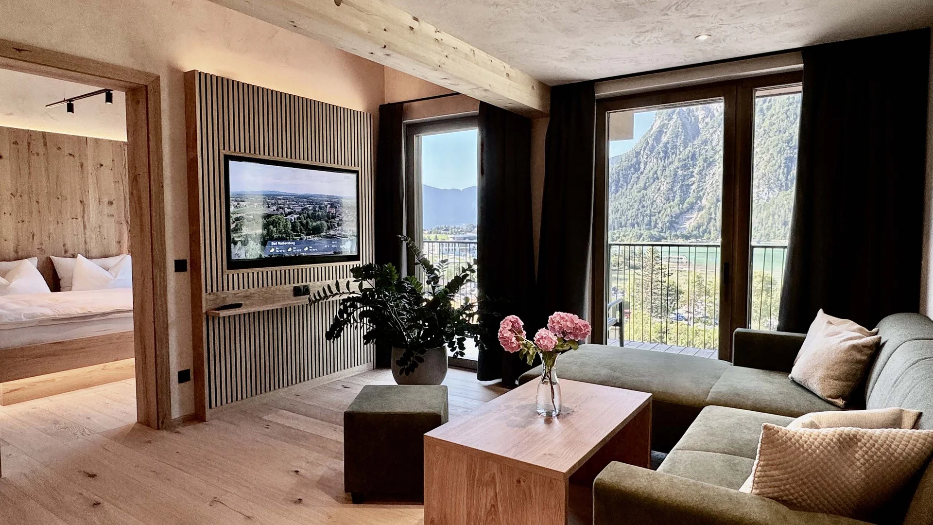 Zimmer und Angebote am Achensee Modernes Wohnzimmer mit grüner Couch, Holzboden und Bergblick durch große Fenster