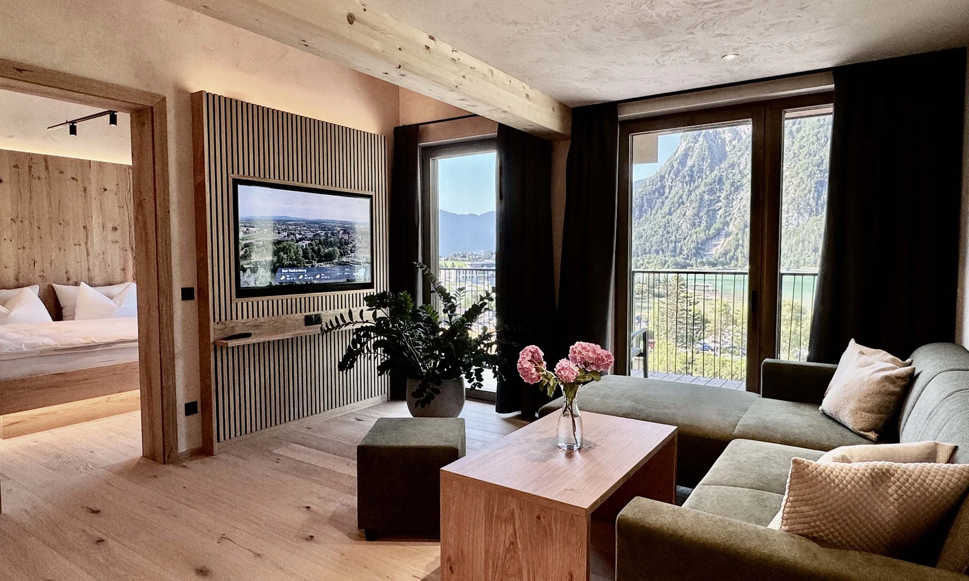 Welcome to our family hotel at Lake Achensee. Modern living room with green sofa, wooden floor and mountain view through large windows