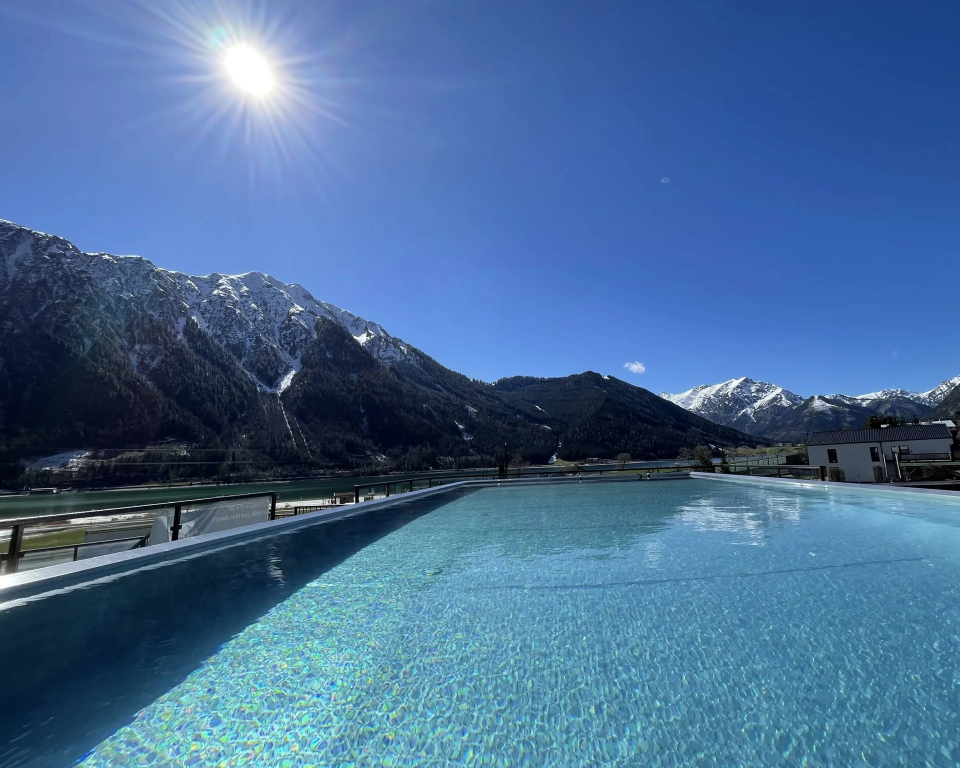 Erholungsurlaub für Eltern Blick auf einen Pool mit Berglandschaft und Sonnenschein bei klarem Himmel