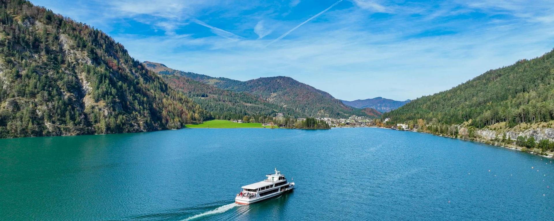 Ihr unvergesslicher Aktivurlaub in Österreich am See Fähre auf blauem See umgeben von bewaldeten Bergen unter blauem Himmel