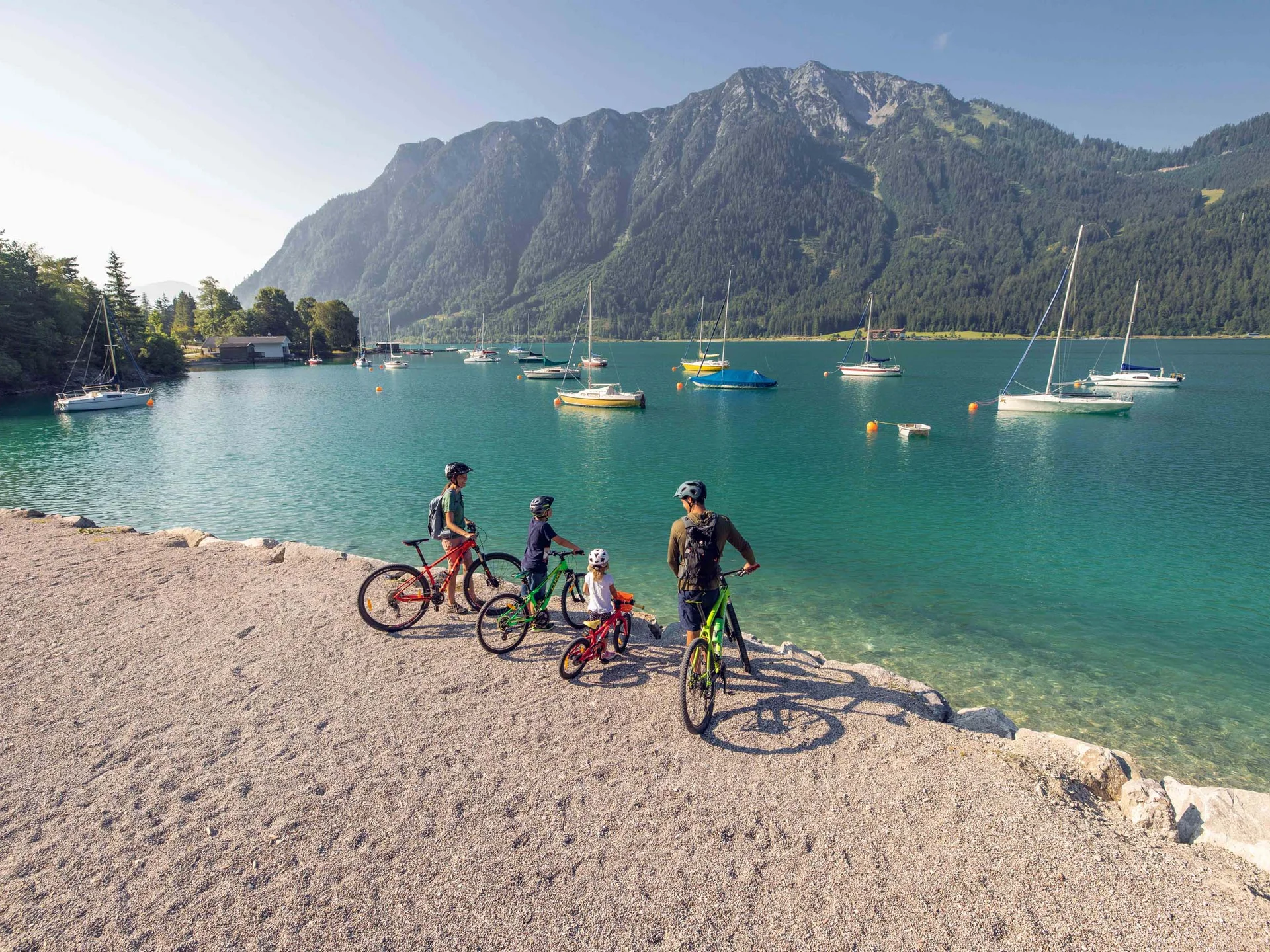 Radtouren für Groß und Klein: Ihr Bikehotel in Tirol Familie mit Fahrrädern am Seeufer vor Bergen und segelbooten