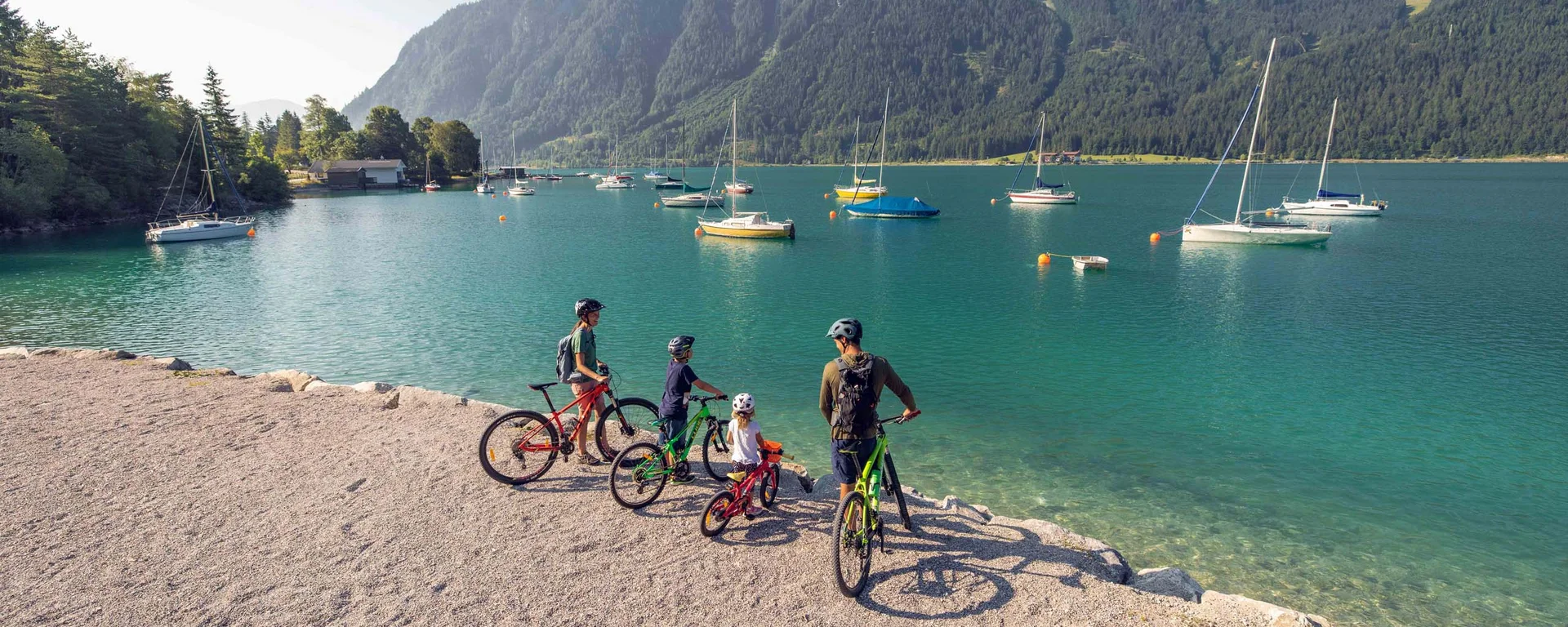 Vom Wanderhotel in Tirol direkt in die Natur Familie mit Fahrrädern am Seeufer vor Bergen und segelbooten