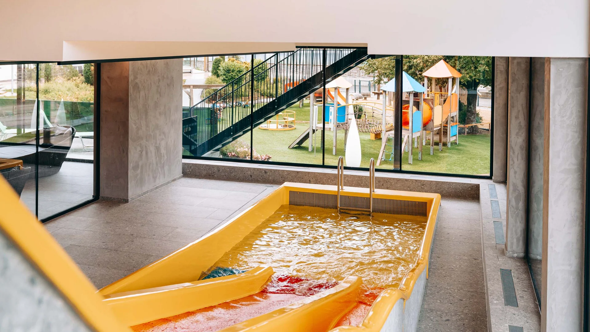 Wasserspaß im Familienhotel in Tirol mit Pool Gelbe Wasserrutsche in Innenbereich mit Blick auf Kinderspielplatz draußen