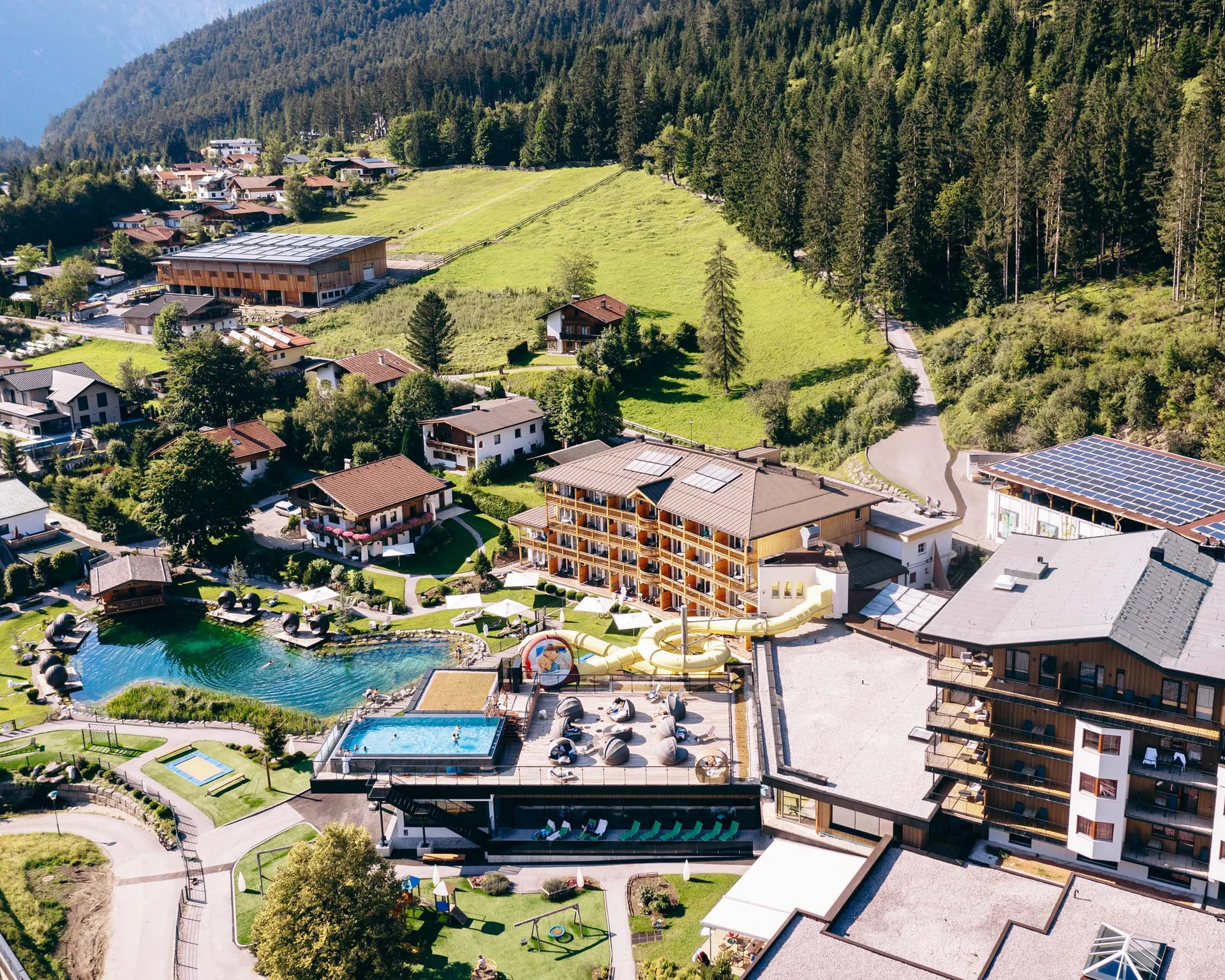 Familienzeit im Kinderhotel Buchau am Achensee Luftaufnahme eines Resorts mit Schwimmbädern, Wasserrutsche und umgeben von Bergen