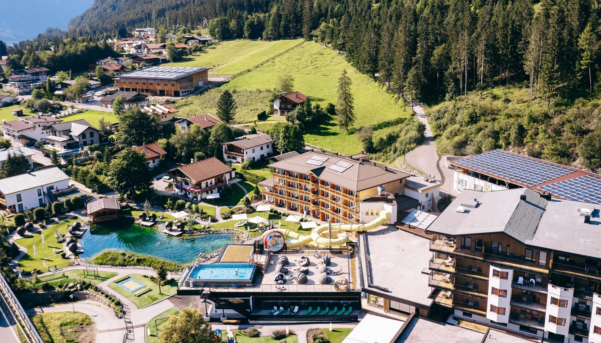 Urlaub im Familienresort in Österreich Luftaufnahme eines Resorts mit Schwimmbädern, Wasserrutsche und umgeben von Bergen