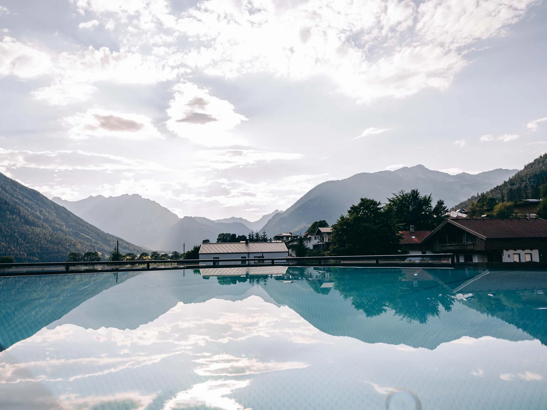 Urlaub im Wellnesshotel mit Kindern in Tirol Berglandschaft mit Häusern und Wasserbecken, das Himmel und Berge spiegelt