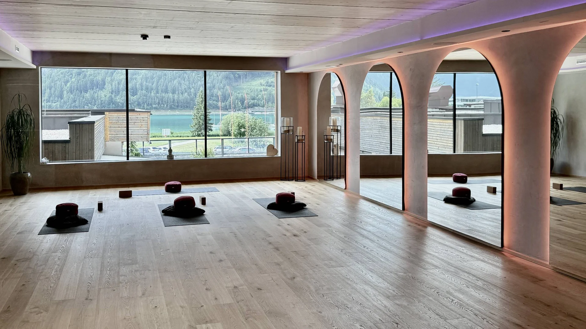 Urlaub im Wellnesshotel mit Kindern in Tirol Helles Yoga-Studio mit Holzboden, Meditationskissen und großer Fensterfront mit Seeblick