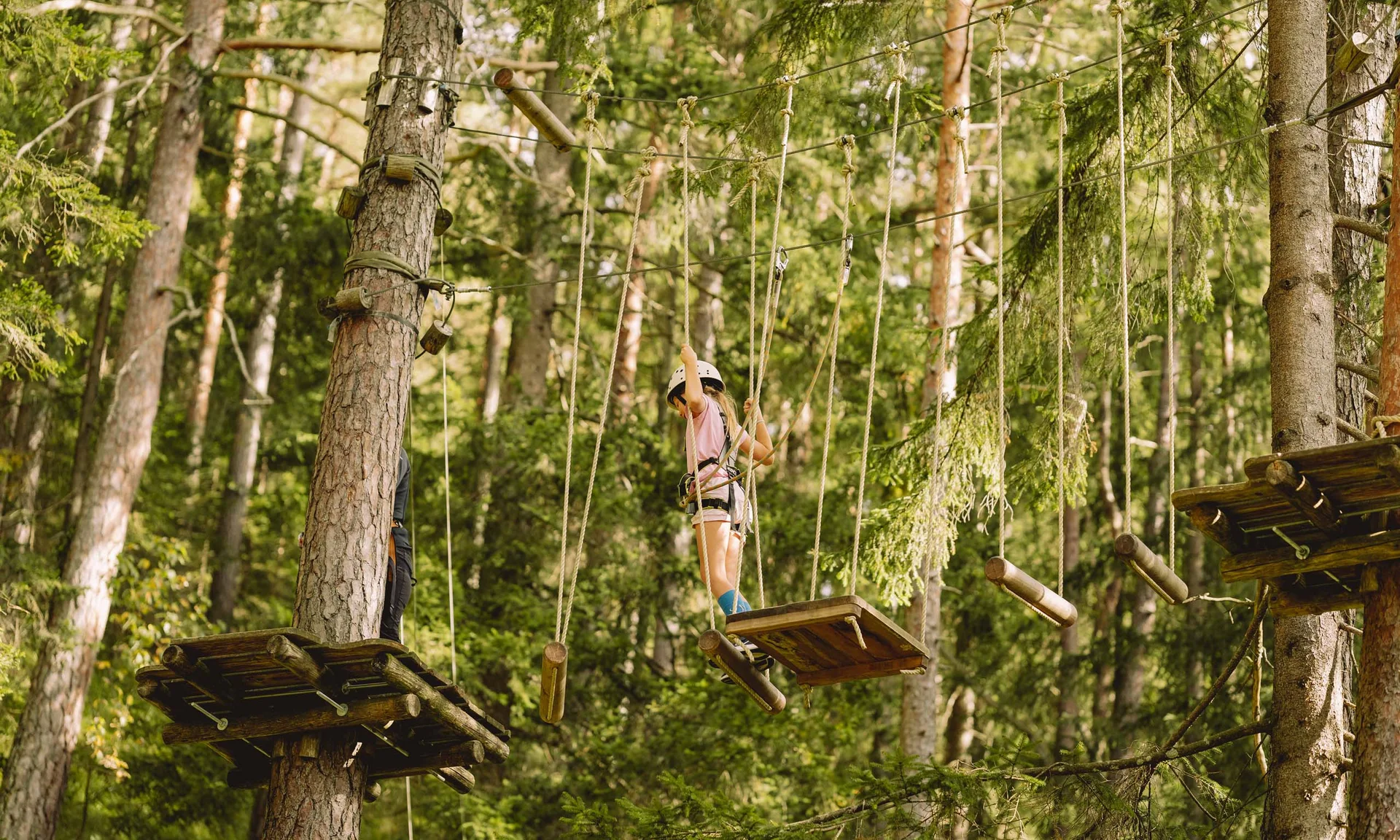 Outdoorspaß im Familienhotel am See in Österreich Kind mit Helm klettert im Hochseilgarten zwischen Bäumen