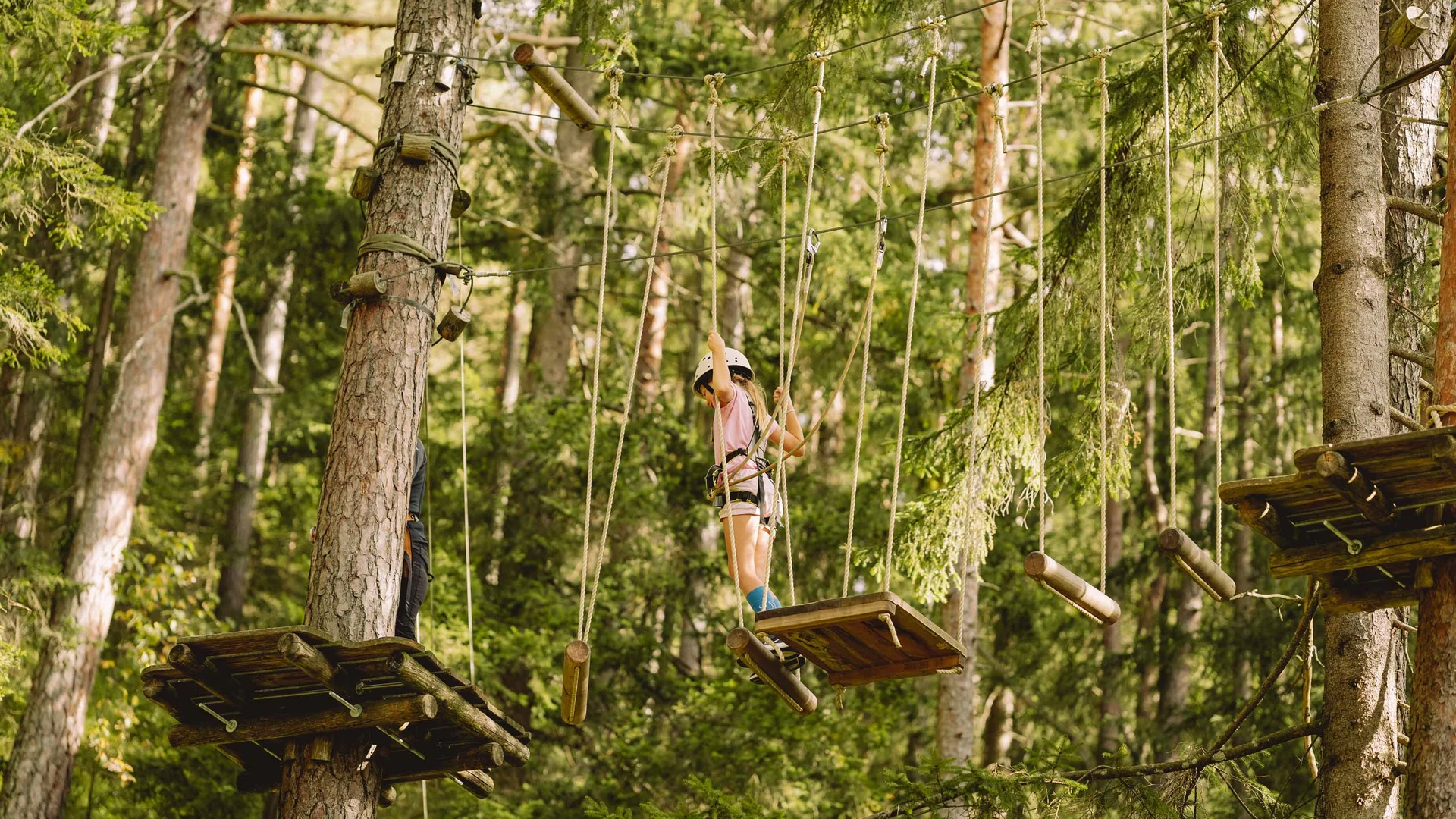 Welcome to our family hotel at Lake Achensee. Child wearing helmet climbing in high ropes course among trees