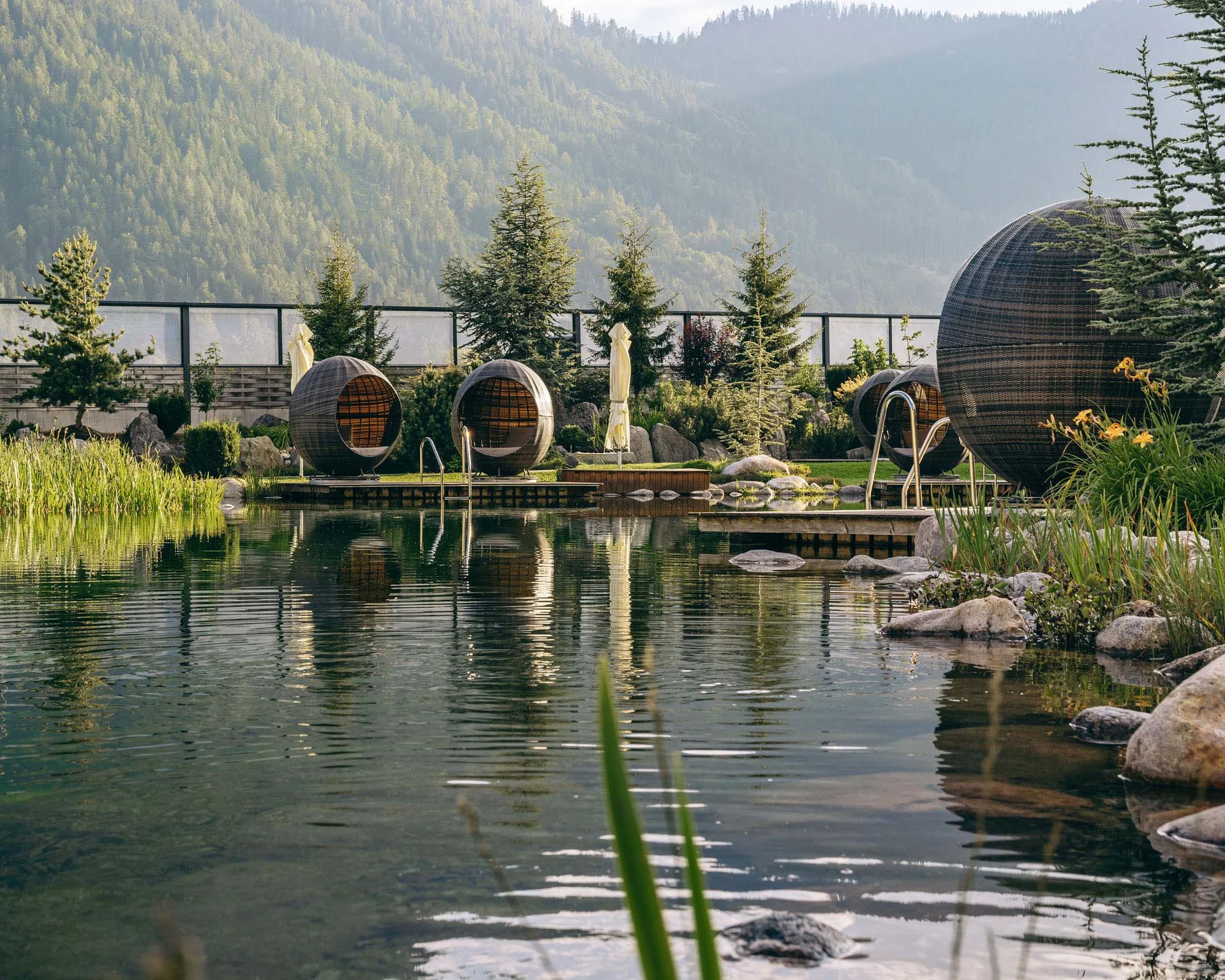 Familienurlaub mit Baby und Kleinkind im Buchau Natürlicher Pool mit runden Sitzpods in einer Gartenanlage mit Bergen im Hintergrund