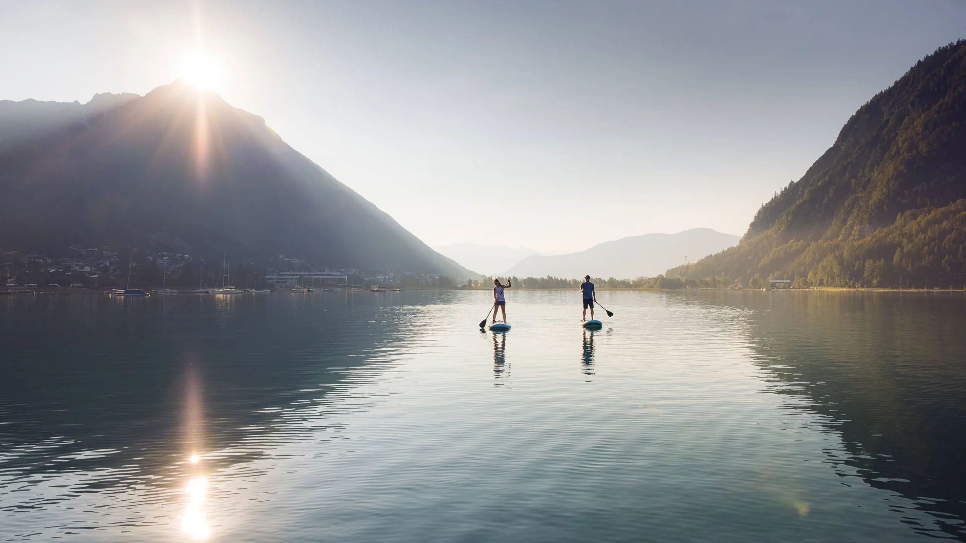 Freizeitkurse für Ihre Kids und Teenies Zwei Personen paddleboarden auf ruhigem Bergsee bei Sonnenaufgang