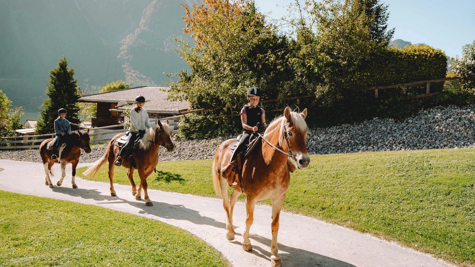 Pferdeglück im Reithotel in Österreich Drei Kinder reiten auf Pferden auf einem Weg vor einer Berglandschaft